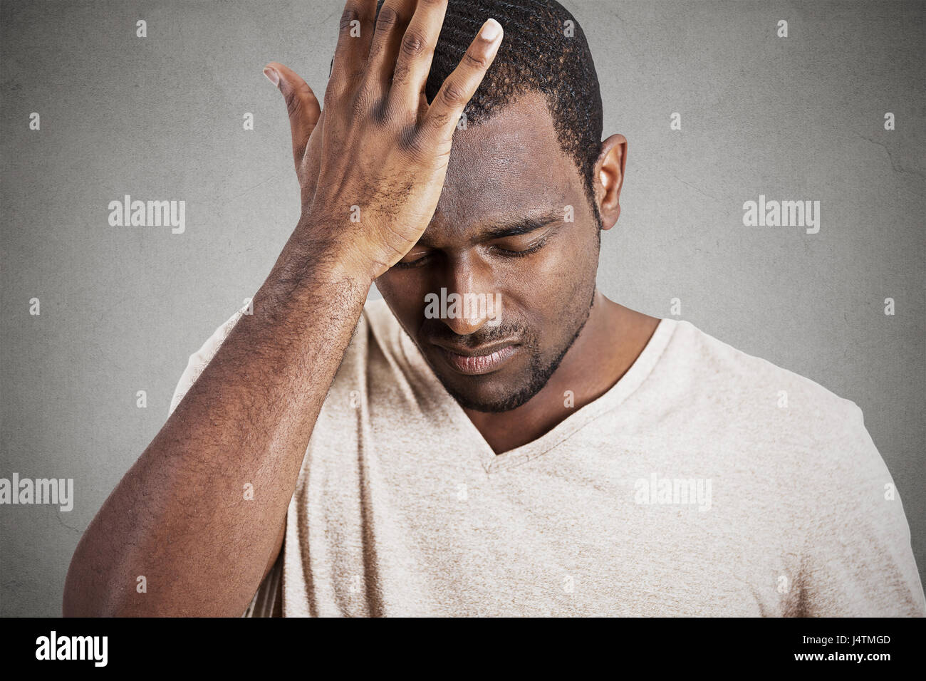 Closeup headshot very sad depressed, stressed, alone, disappointed gloomy young man head on hands having suicidal thoughts isolated grey wall backgrou Stock Photo