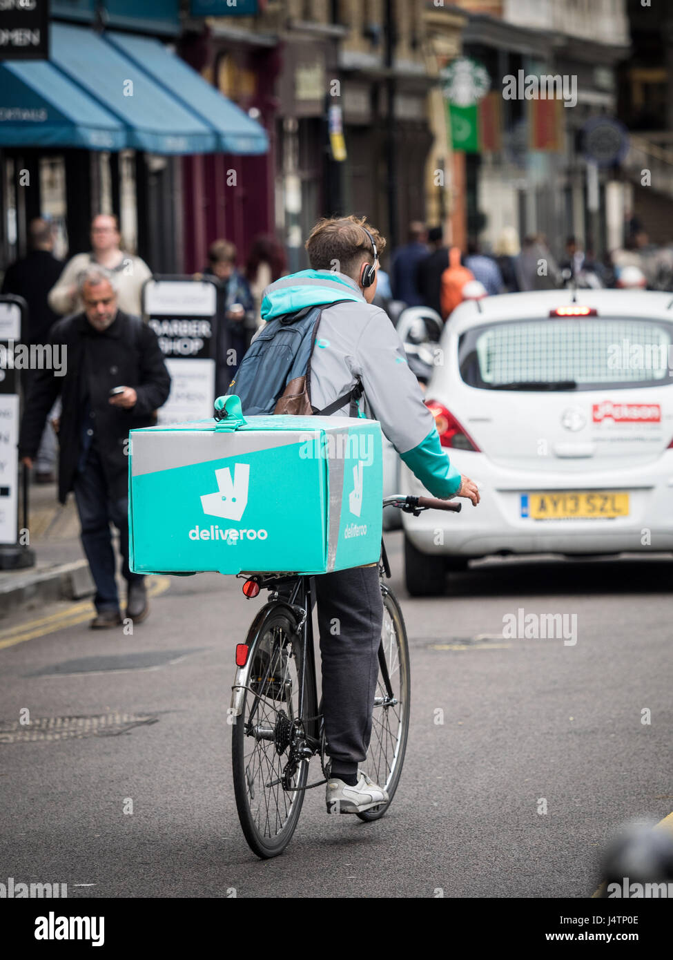 A Deliveroo food delivery courier rides through the streets of Soho in central London Stock Photo