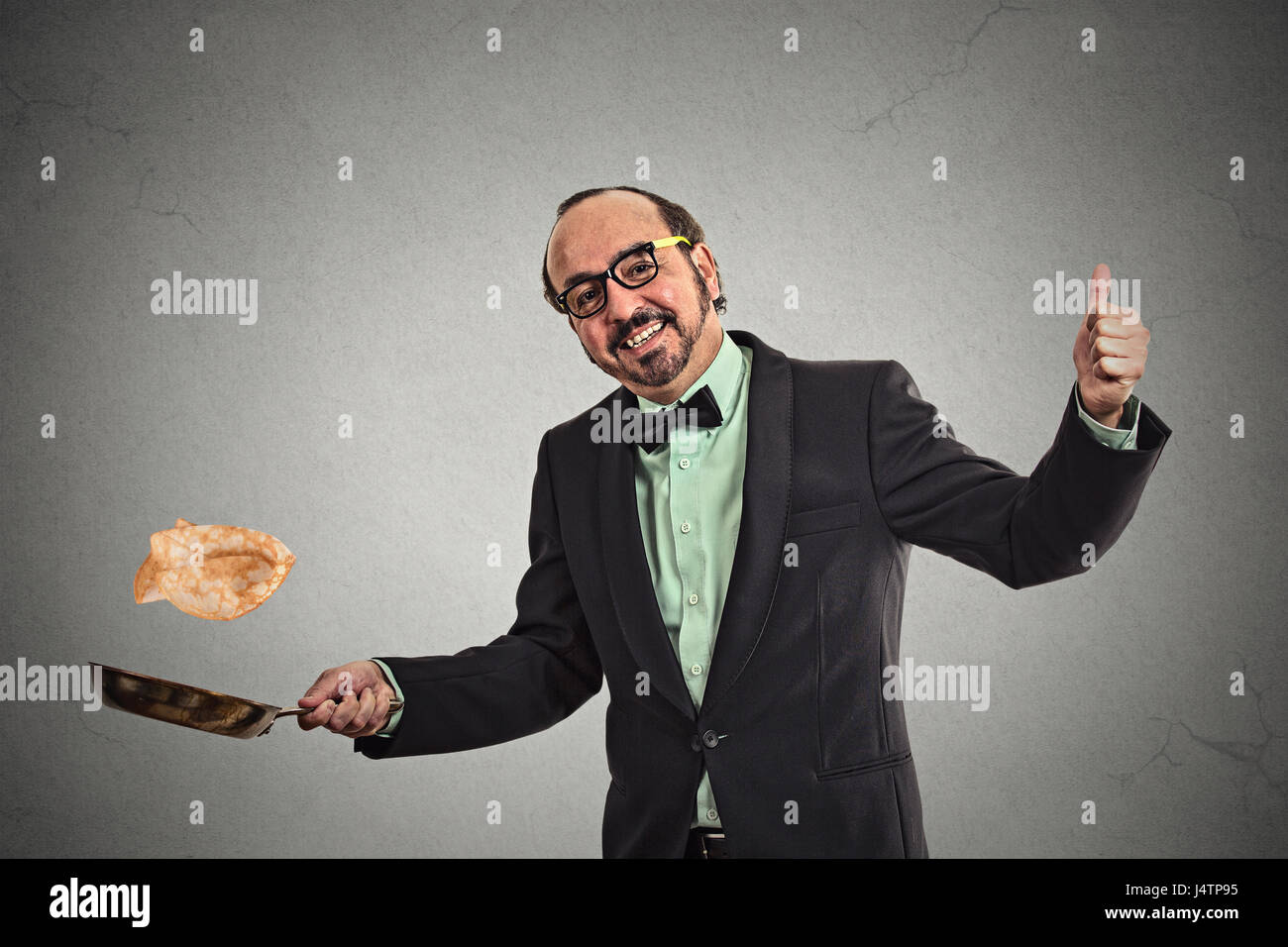 Happy smiling man tossing pancakes on frying pan isolated on grey wall