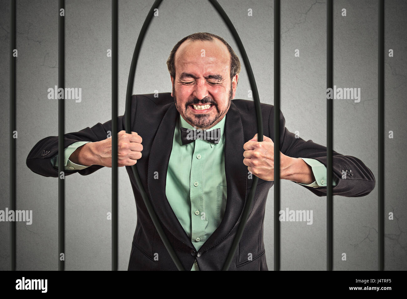 Furious strong middle aged businessman bending bars of his prison cell grey wall background. Life limitations, law violation infringement tax evasion  Stock Photo