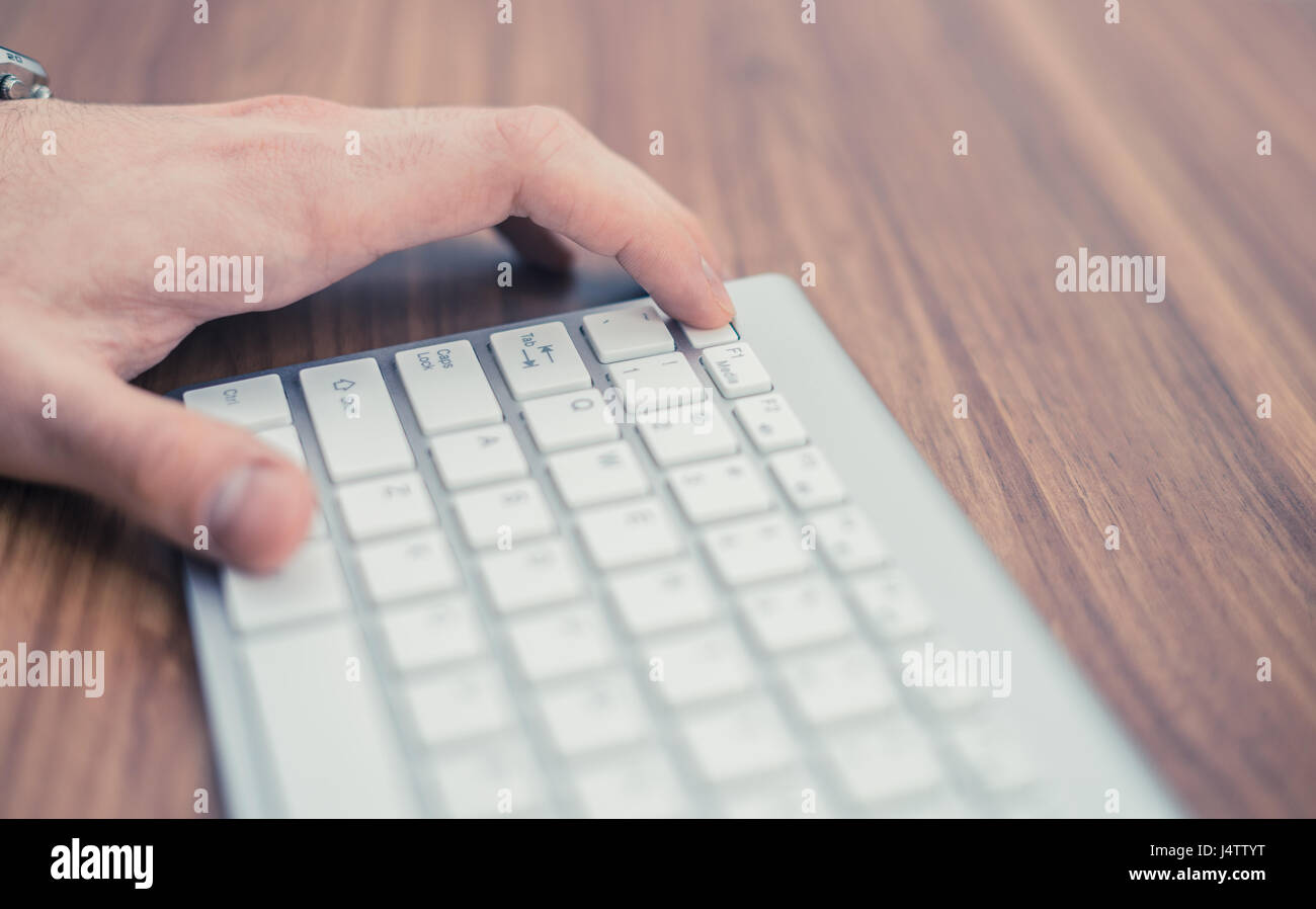 Man's hand pressing escape button on wireless keyboard on wooden table Stock Photo