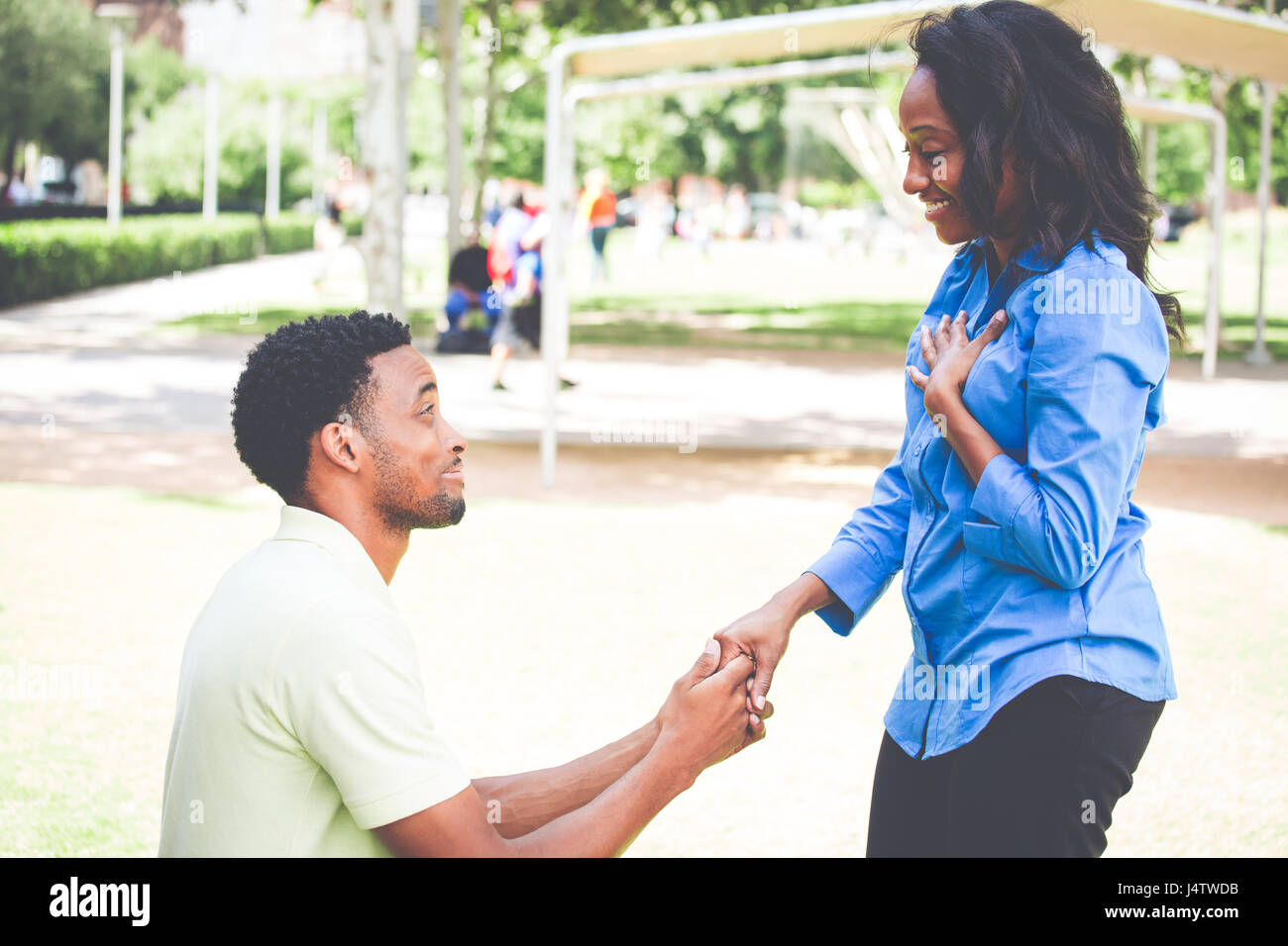 Portrait of young man dropping on knees to propose and lady answering i do, isolated outdoors outside background Stock Photo