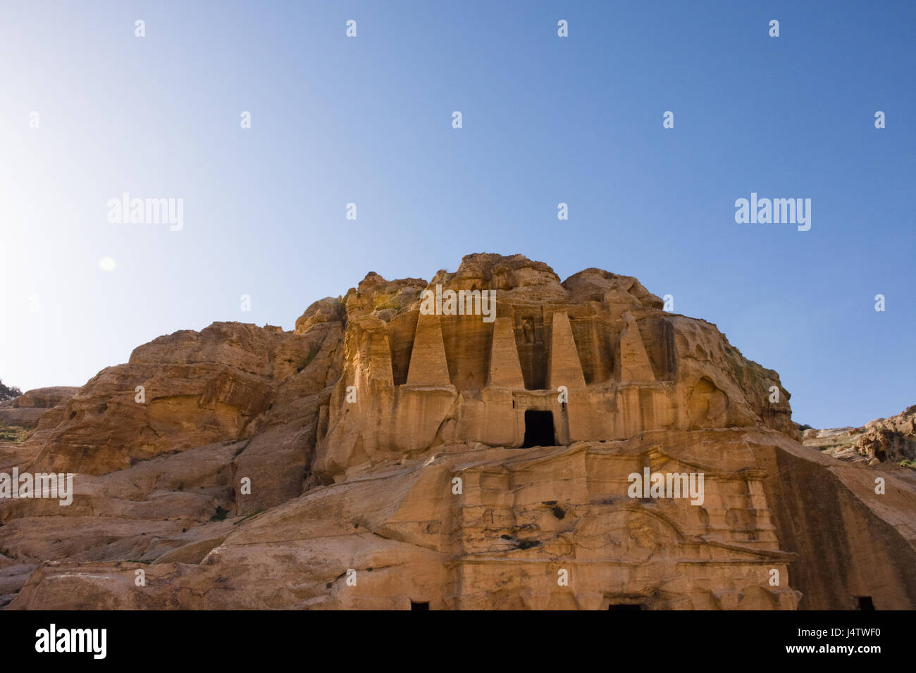Carved Doric column facade of the Obelisk Tomb, Bab as-Siq, Petra Jordan with the Triclinium beneath it. Photographed from below with blue sky above. Stock Photo