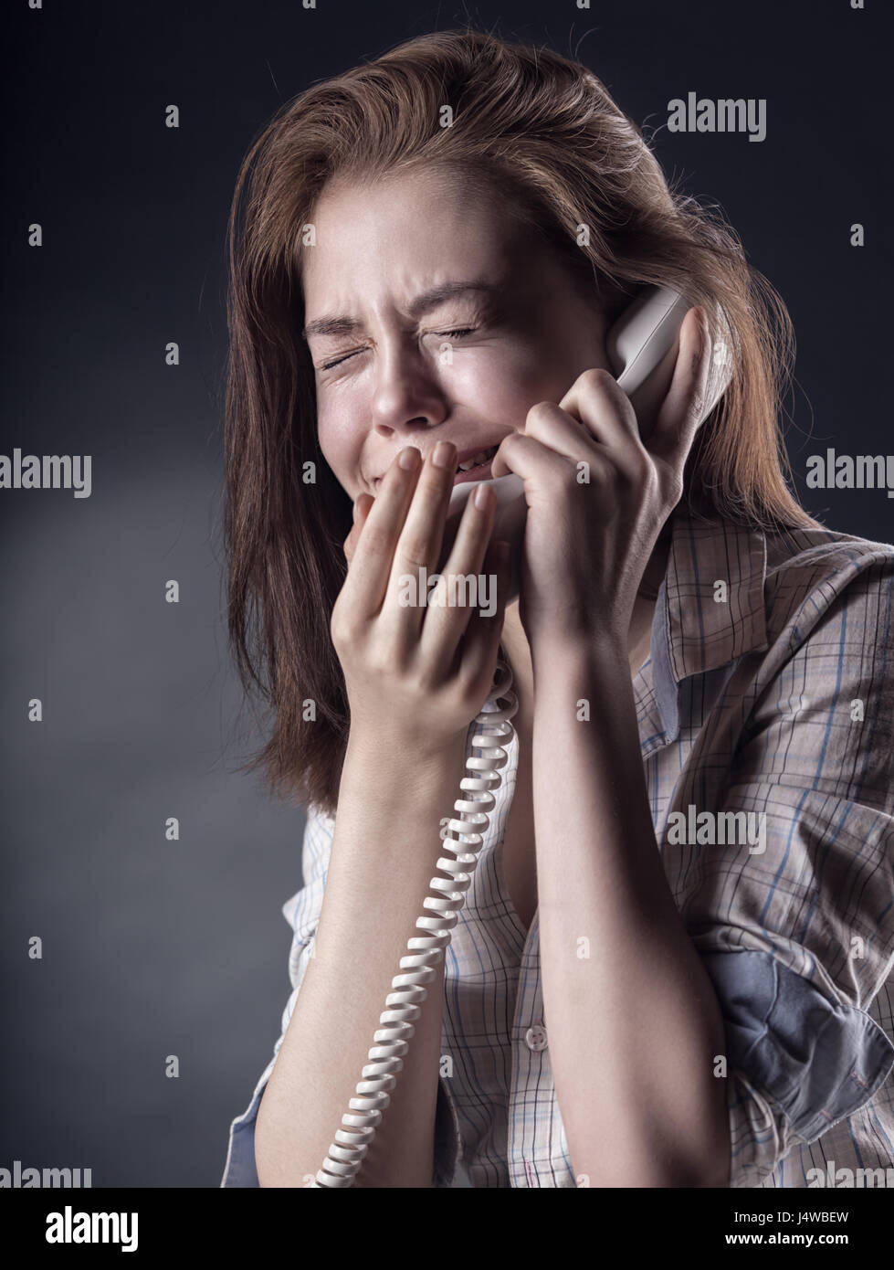 Crying young woman with a phone on a dark background Stock Photo