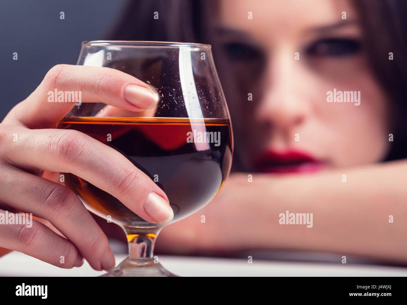 Woman in depression, drinking alcohol. Focus on glass Stock Photo