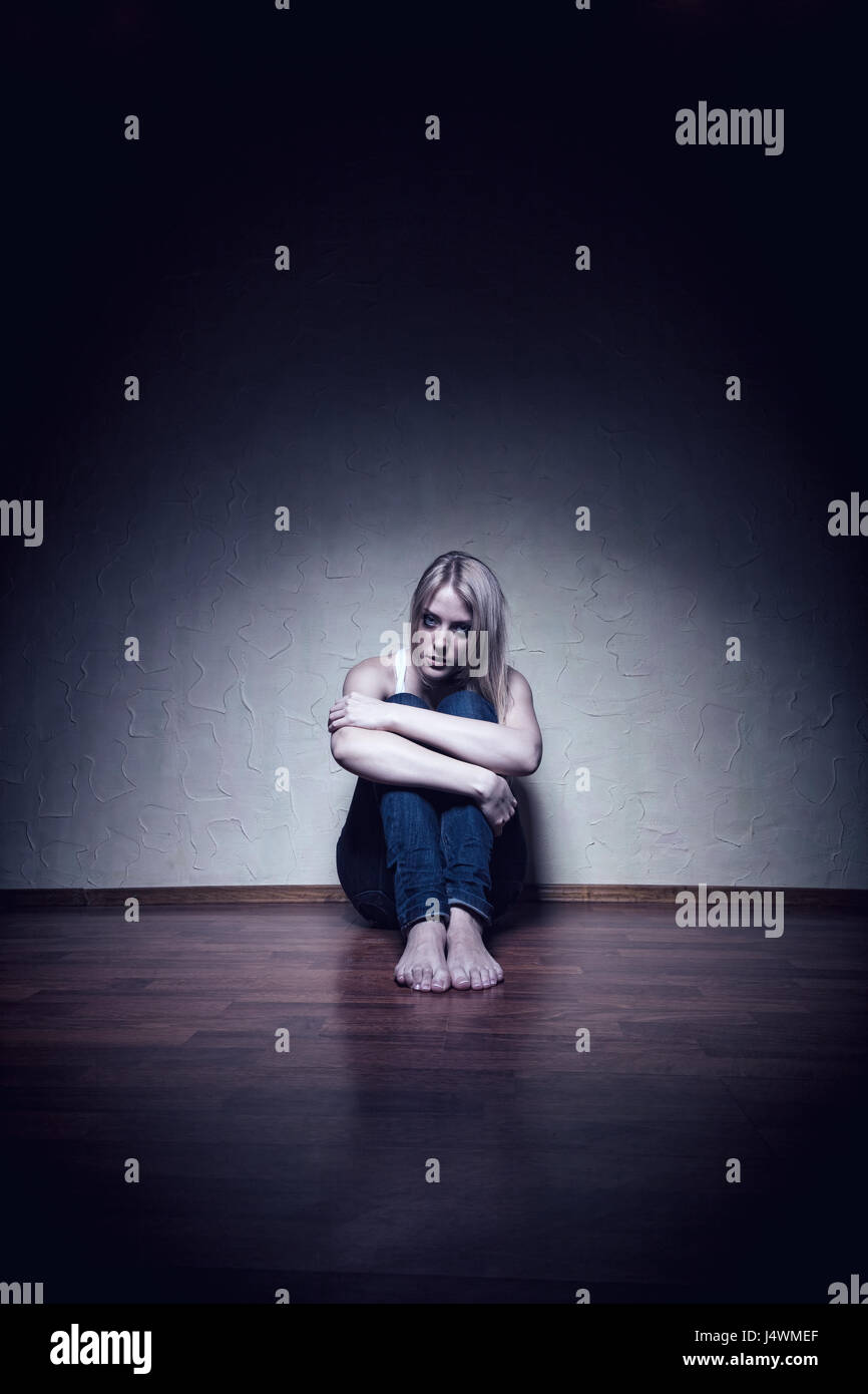 Young sad woman sitting alone on the floor in an empty room Stock Photo