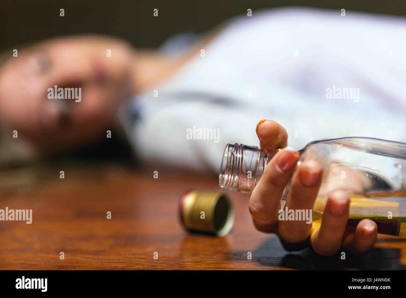 Drunken young woman lying on the floor. Focus on the bottle Stock Photo