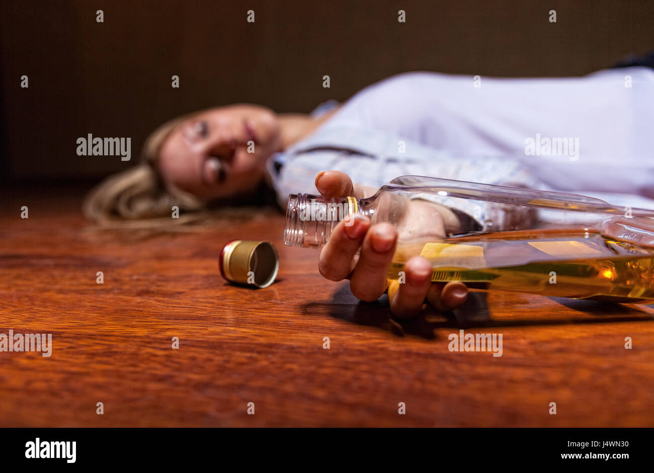 Drunken young woman lying on the floor. Focus on the bottle Stock Photo