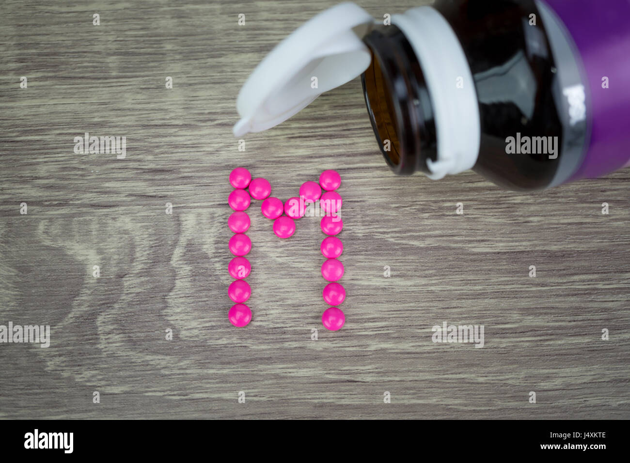 Pink pills forming shape to M alphabet on wood background Stock Photo