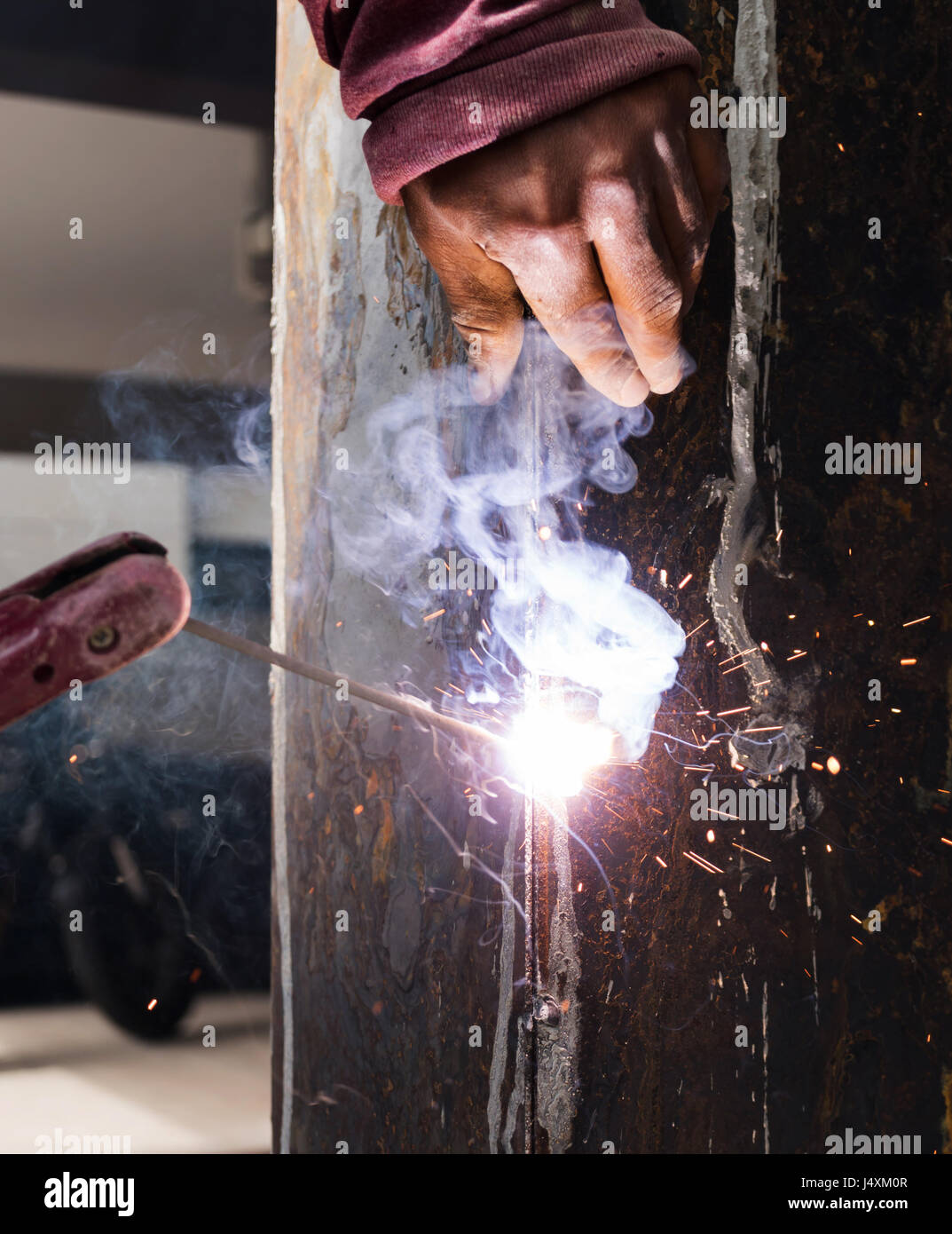 Worker welding steel with spark lighting and smoke at construction site Stock Photo