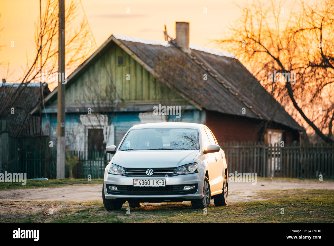 Gomel, Belarus - April 9, 2017: Volkswagen Polo Car Parking On Country Road On A Background Of Traditional Old Wooden Village House In Sunny Evening Stock Photo