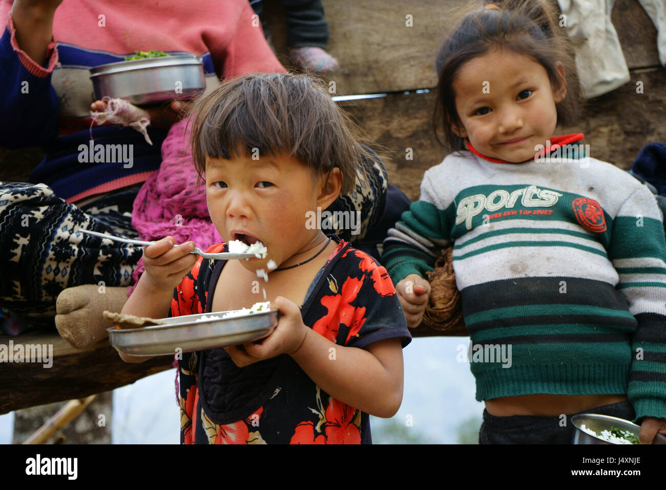 Child eating lunch during break of mothers crushing rocks with hammers for road construction, Yuksam, Sikkim, India Stock Photo