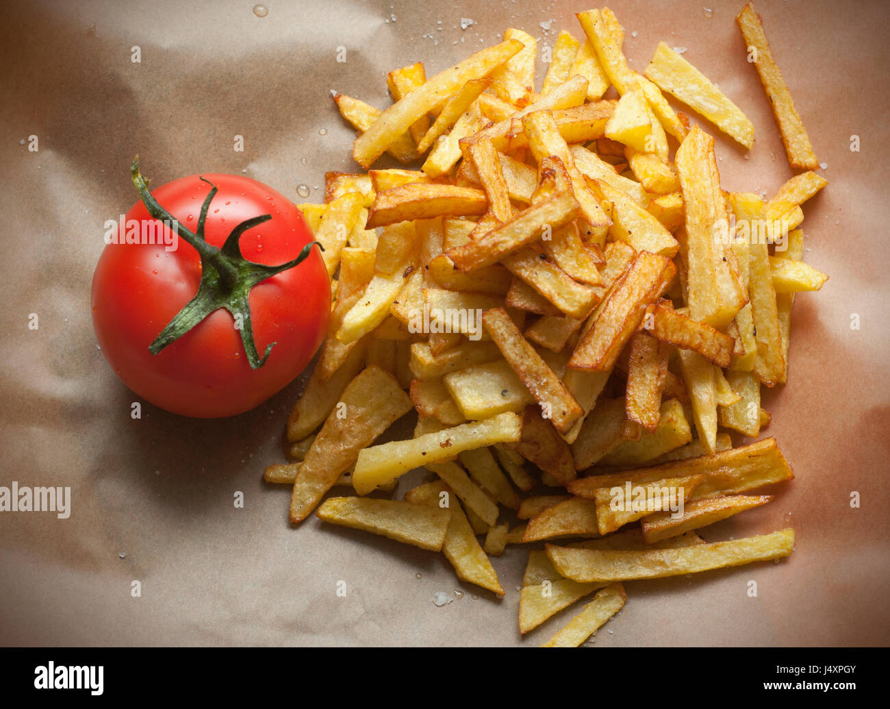 Homemade fried potatoes and one tomato on brown paper Stock Photo