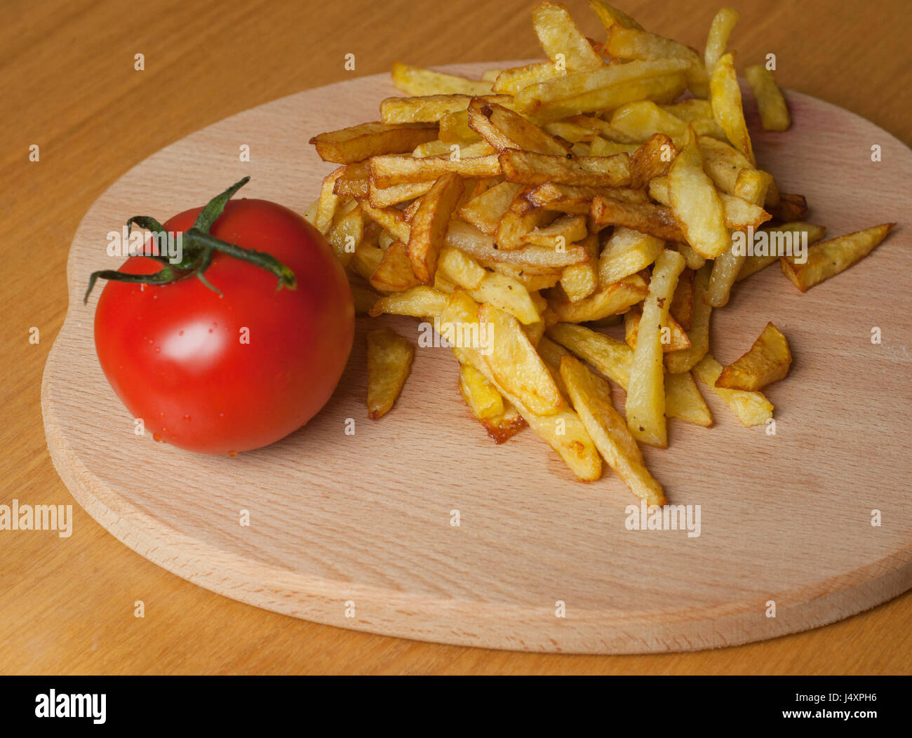 French fried potatoes and one tomato on wooden board Stock Photo