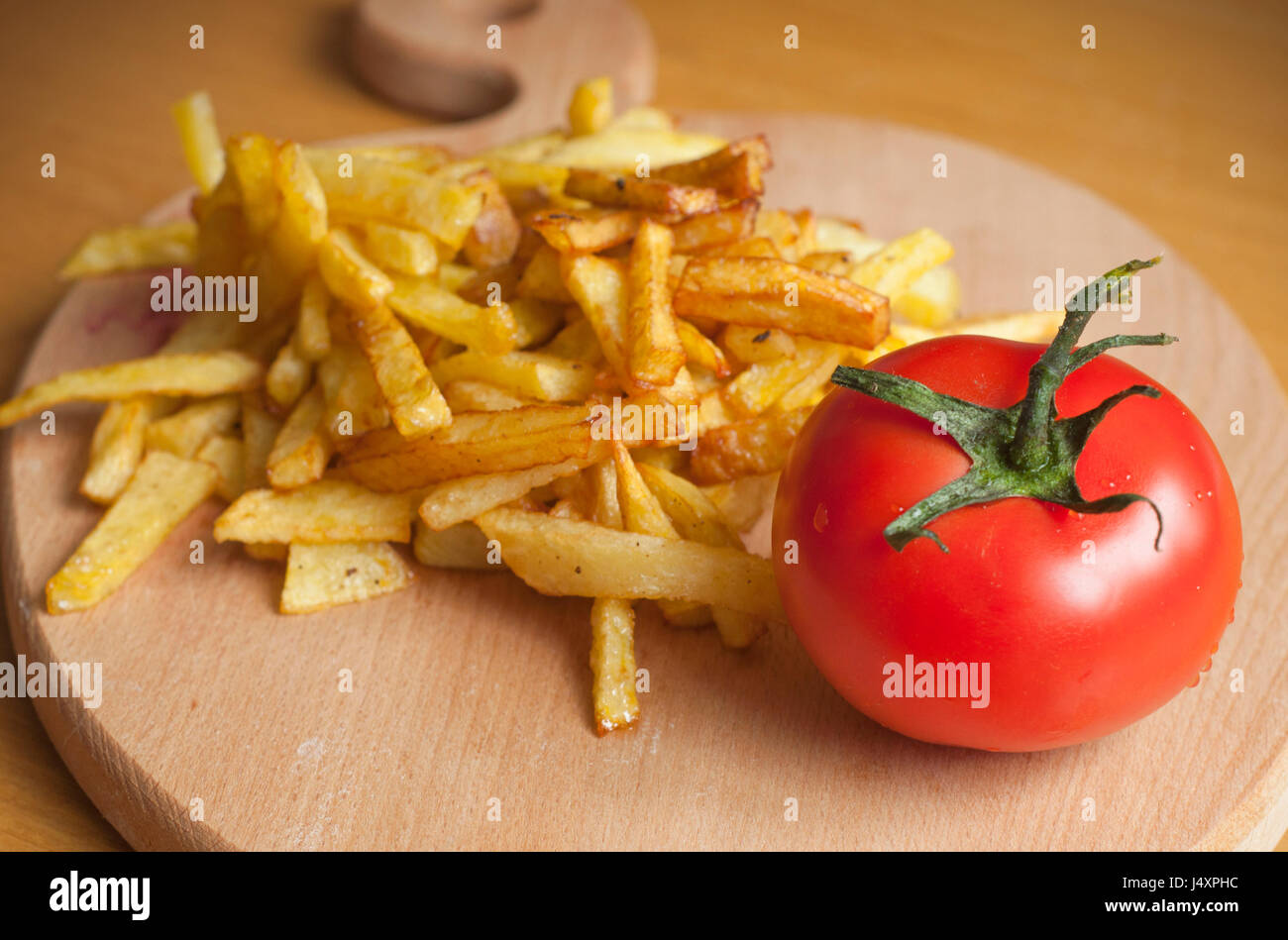 French fried potatoes and one tomato on wooden board Stock Photo