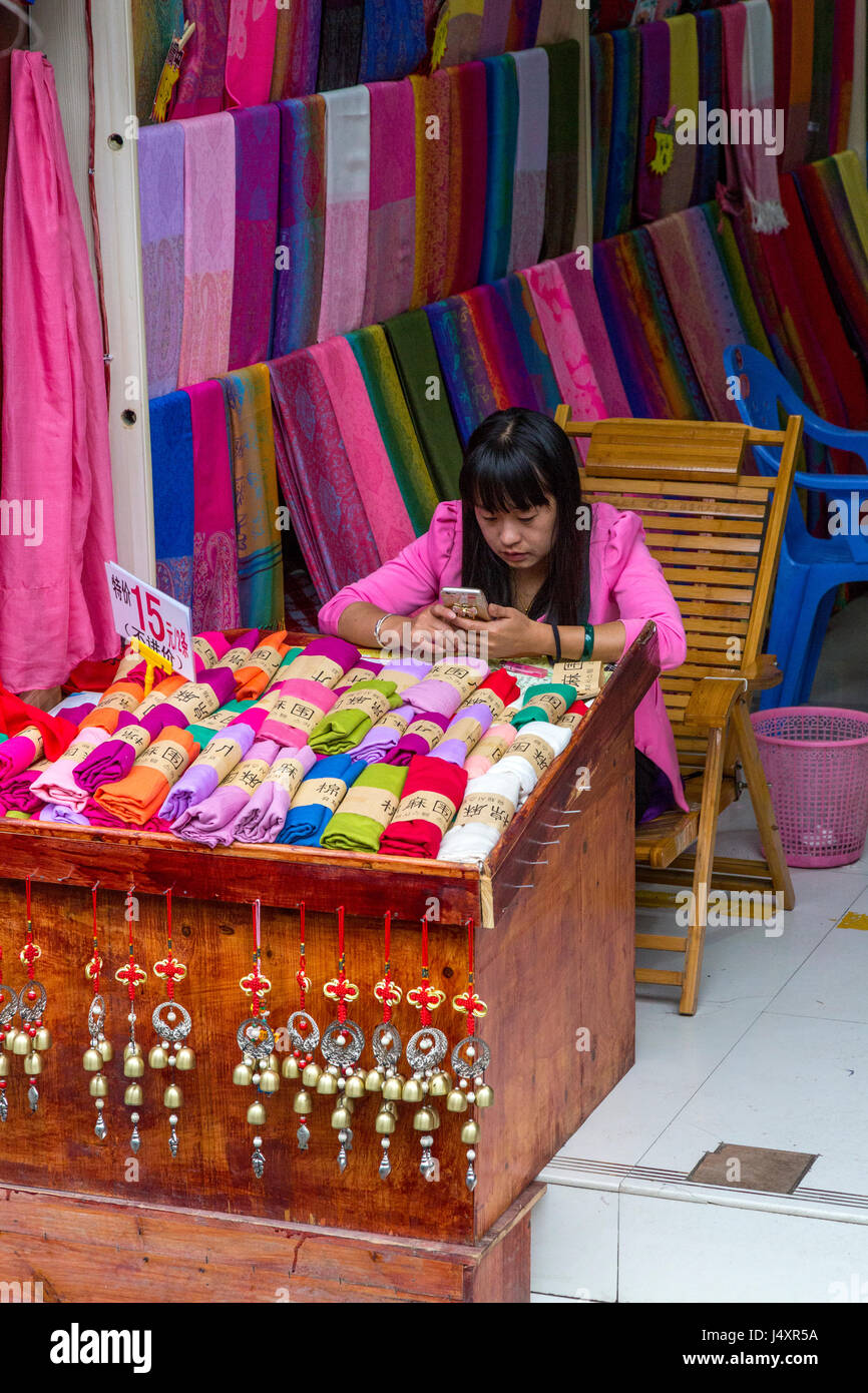 Zhenyuan, Guizhou, China.  Fabric Store Clerk Checking her Cell Phone. Stock Photo