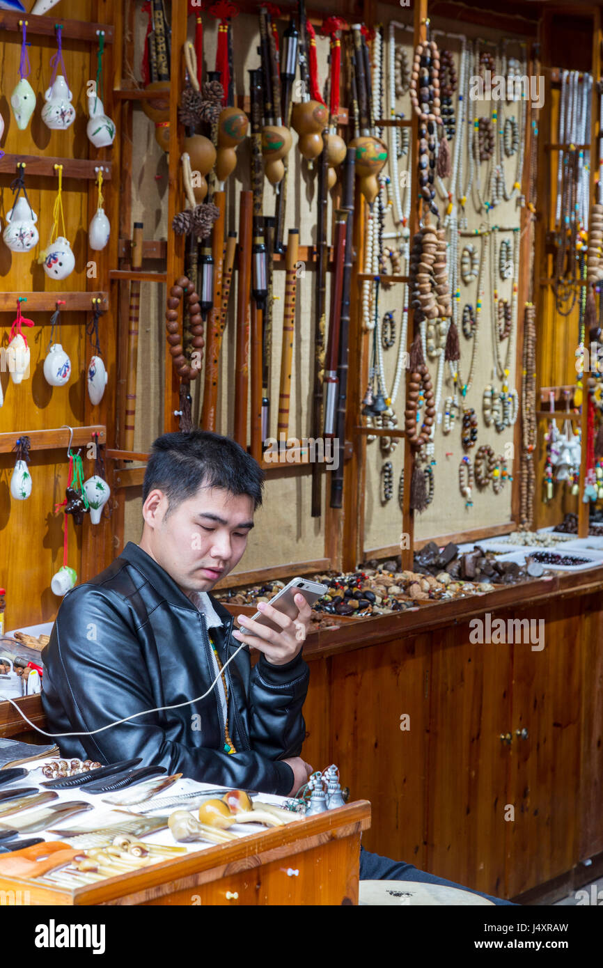Zhenyuan, Guizhou, China.  Shopkeeper Checking his Cell Phone. Stock Photo