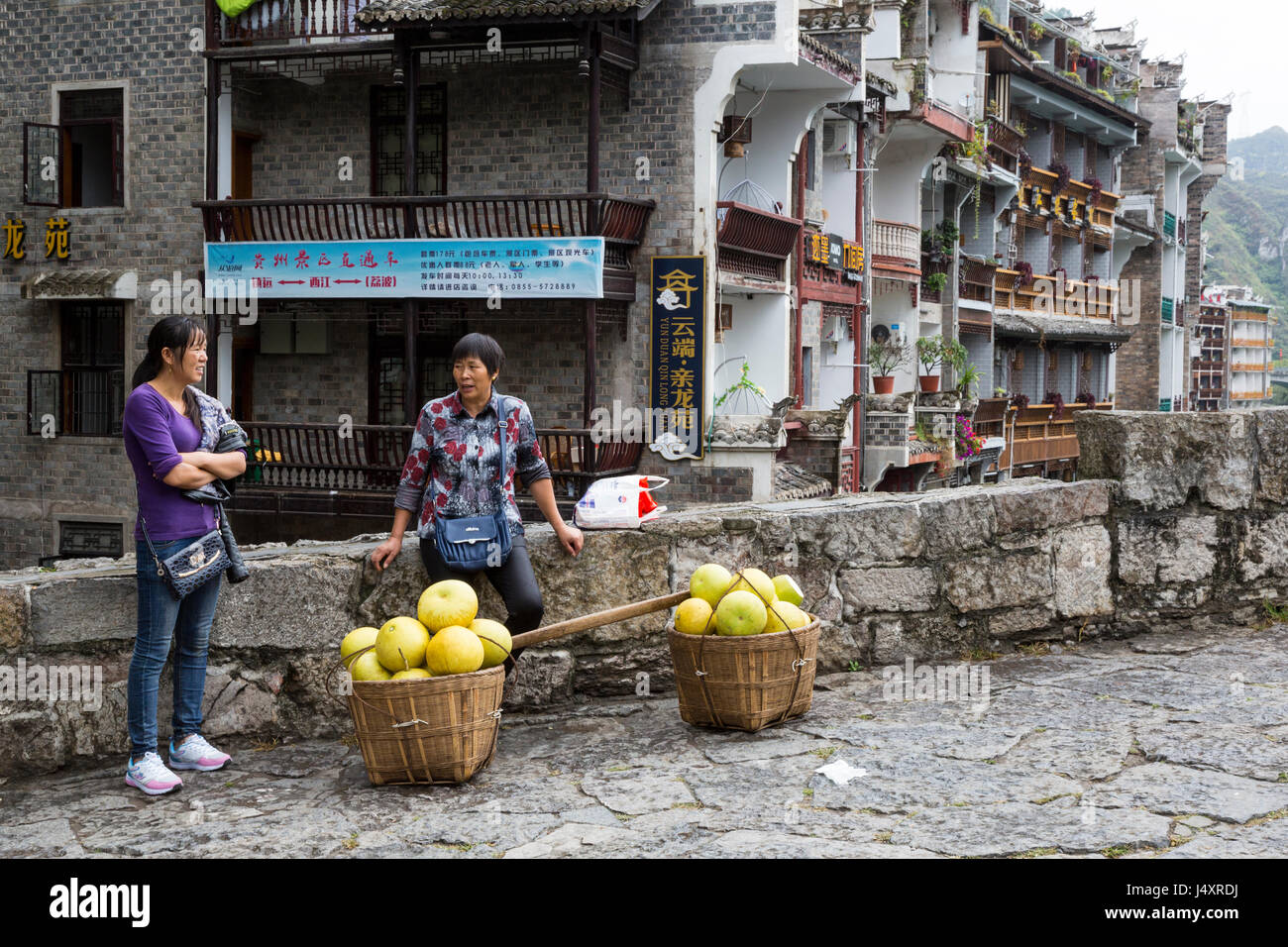 Zhenyuan, Guizhou, China.  Pomelo Vendor Talking to Friend on the Zhusheng Bridge. Stock Photo