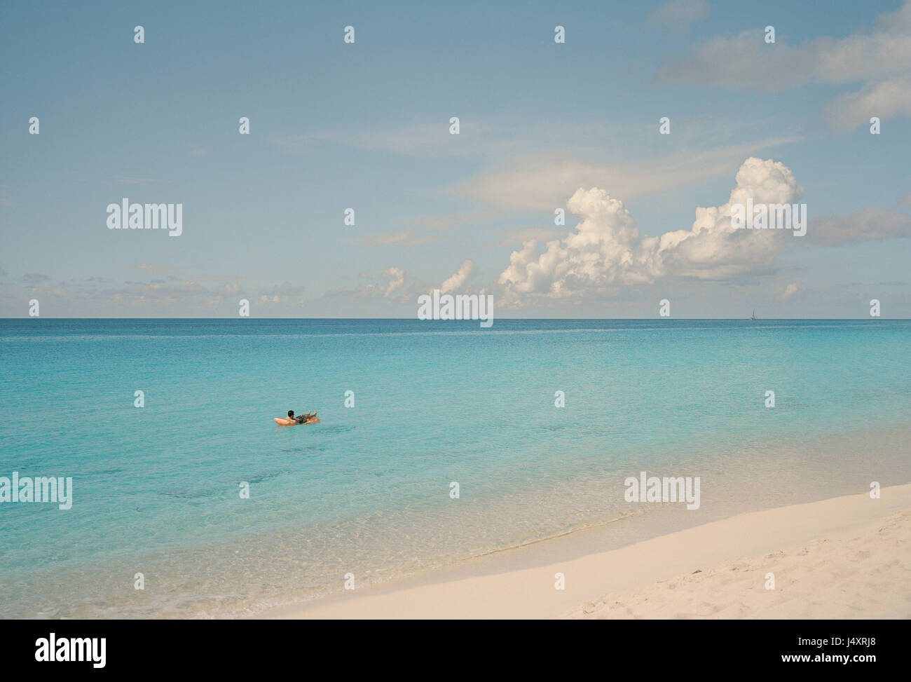 A lone bather on an inflatable bed floats in the azur waters off a beach in Saint Martin, an island in the Caribbean sea.  Derek Hudson / Alamy Stock  Stock Photo