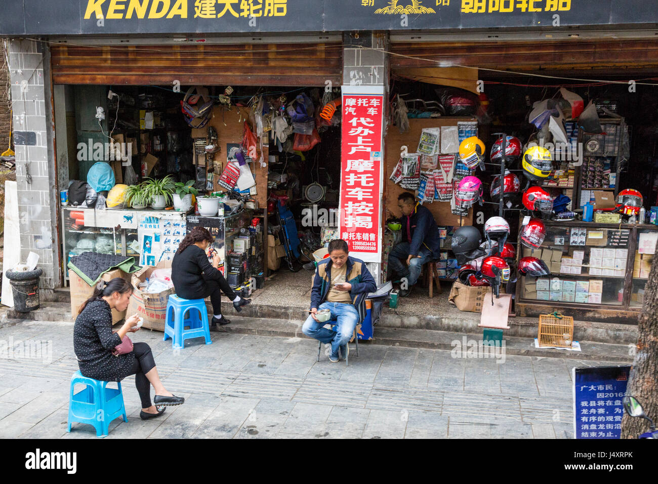 Zhenyuan, Guizhou, China.  People Eating in Front of Motorbike Parts Supply Store. Stock Photo