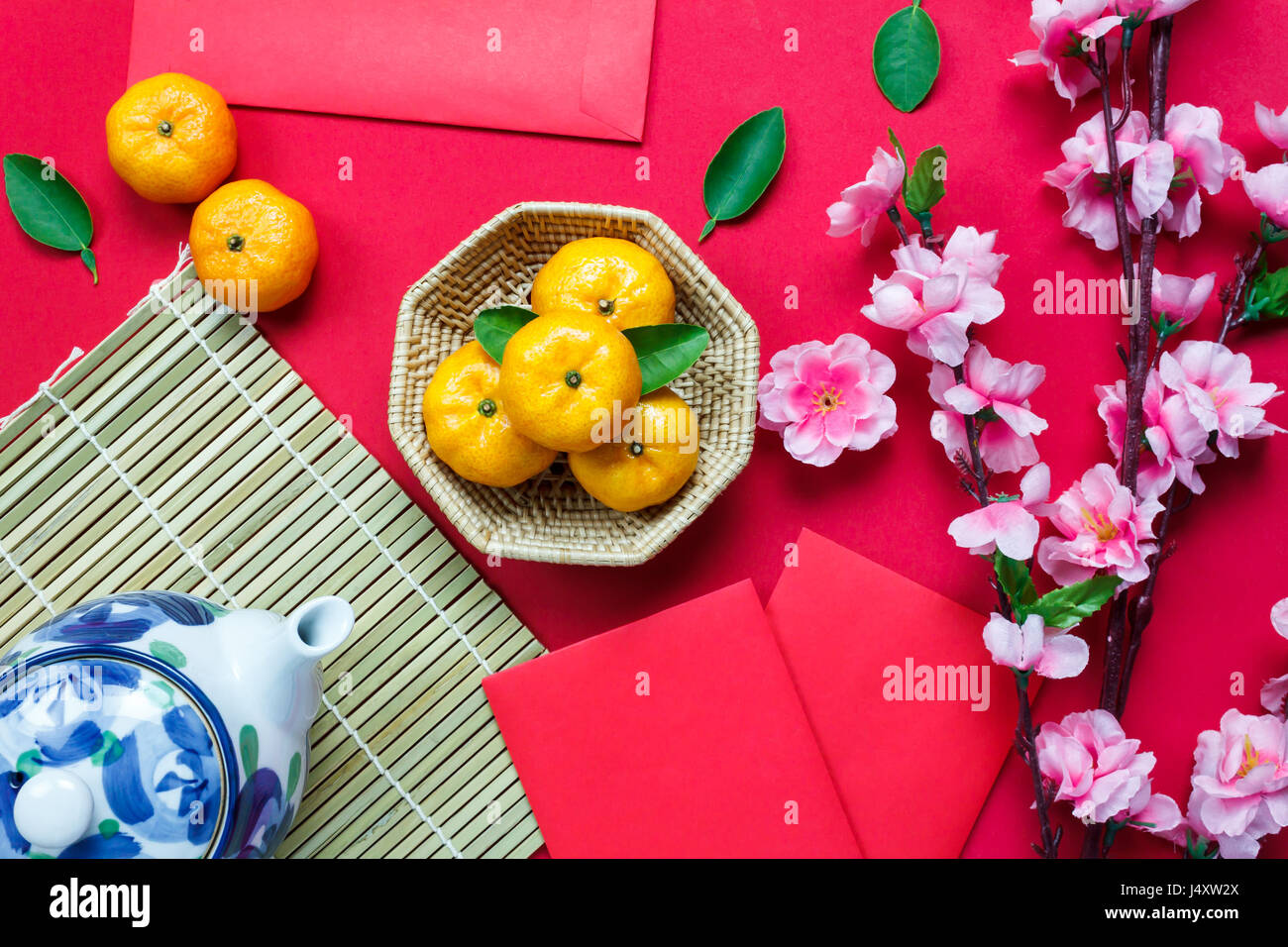 Top view accessories Chinese new year festival decorations.orange,leaf,wood basket,red packet,plum blossom,teapot on red background. Stock Photo