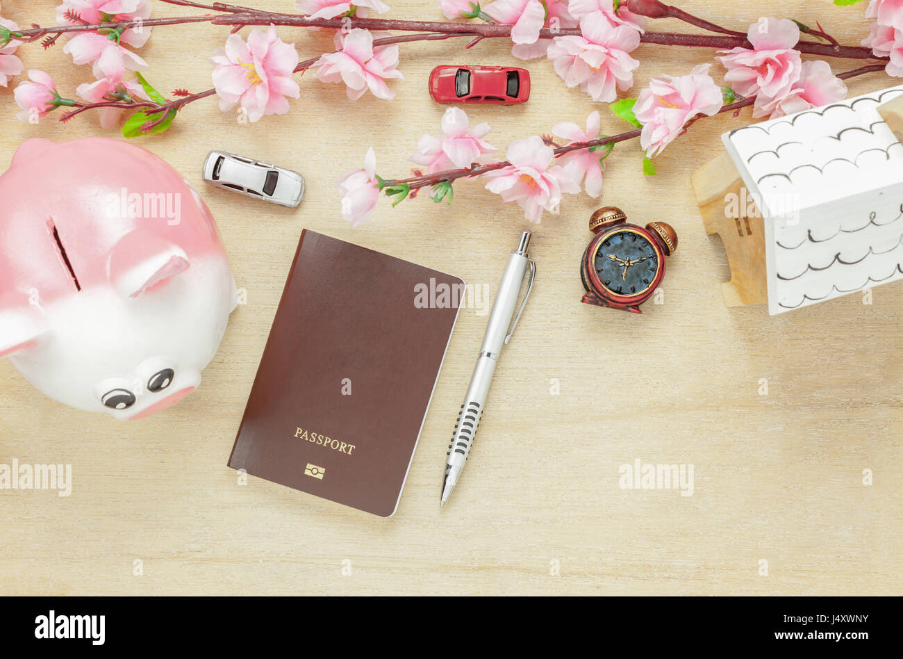 Top view business office desk concept. Saving money to travel with passport.Wood house  also car and clock on wooden shelf.The beautiful pink flower w Stock Photo