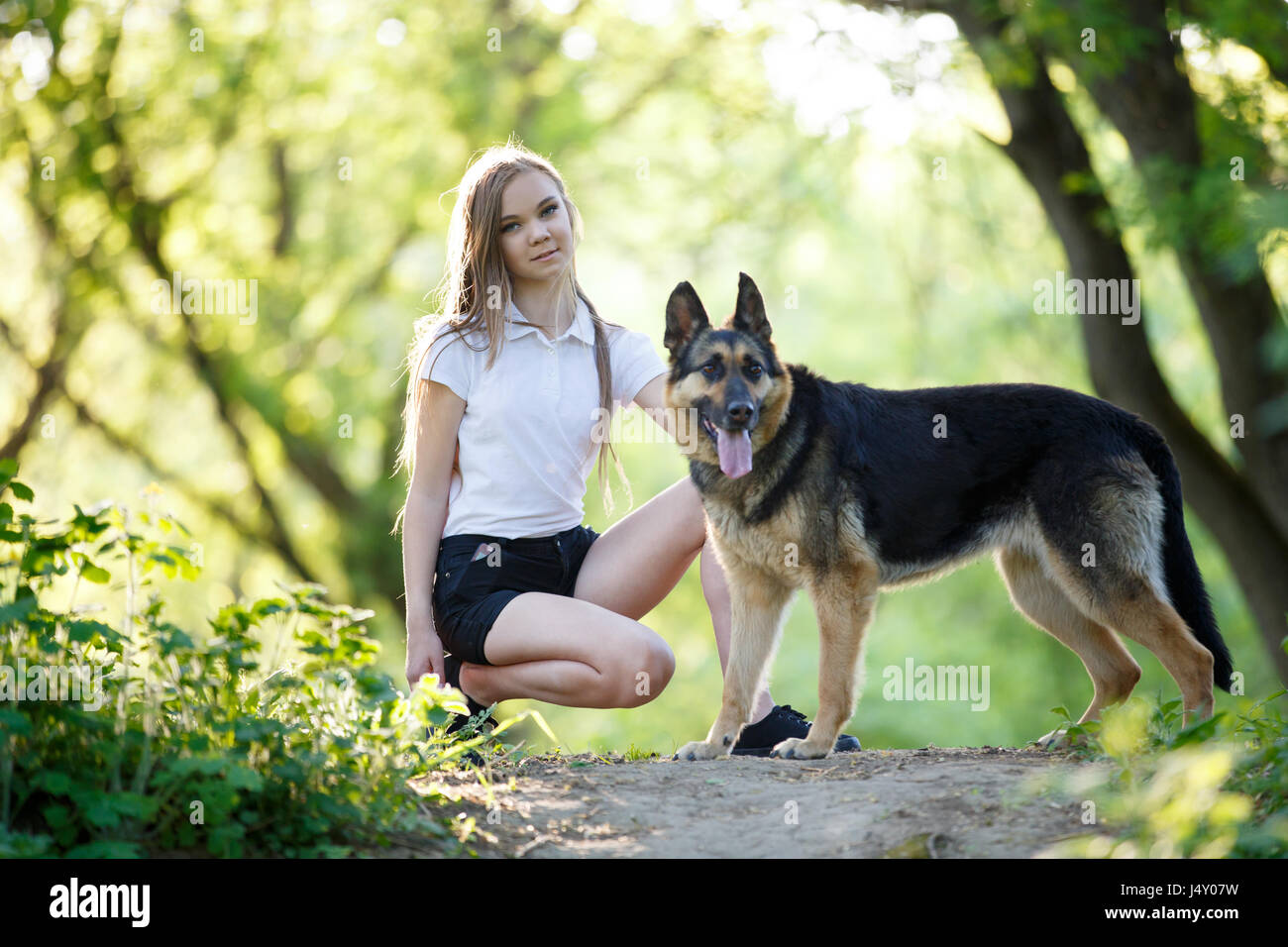 Teenage girl in white shirt with her dog sitting on pathway in the park ...