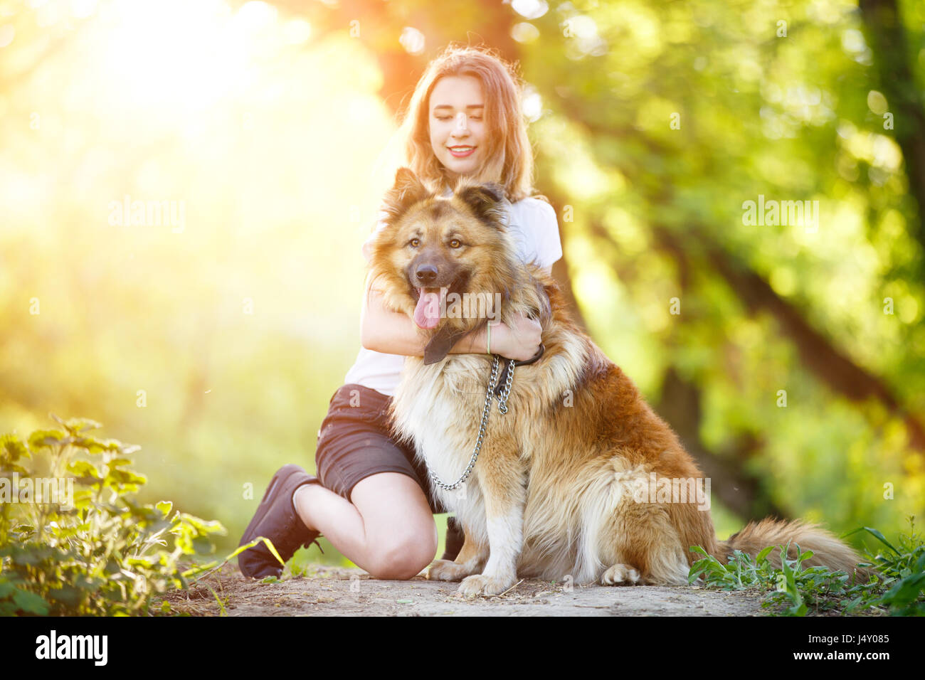 Teenage girl in white shirt with her dog sitting on pathway in the park ...