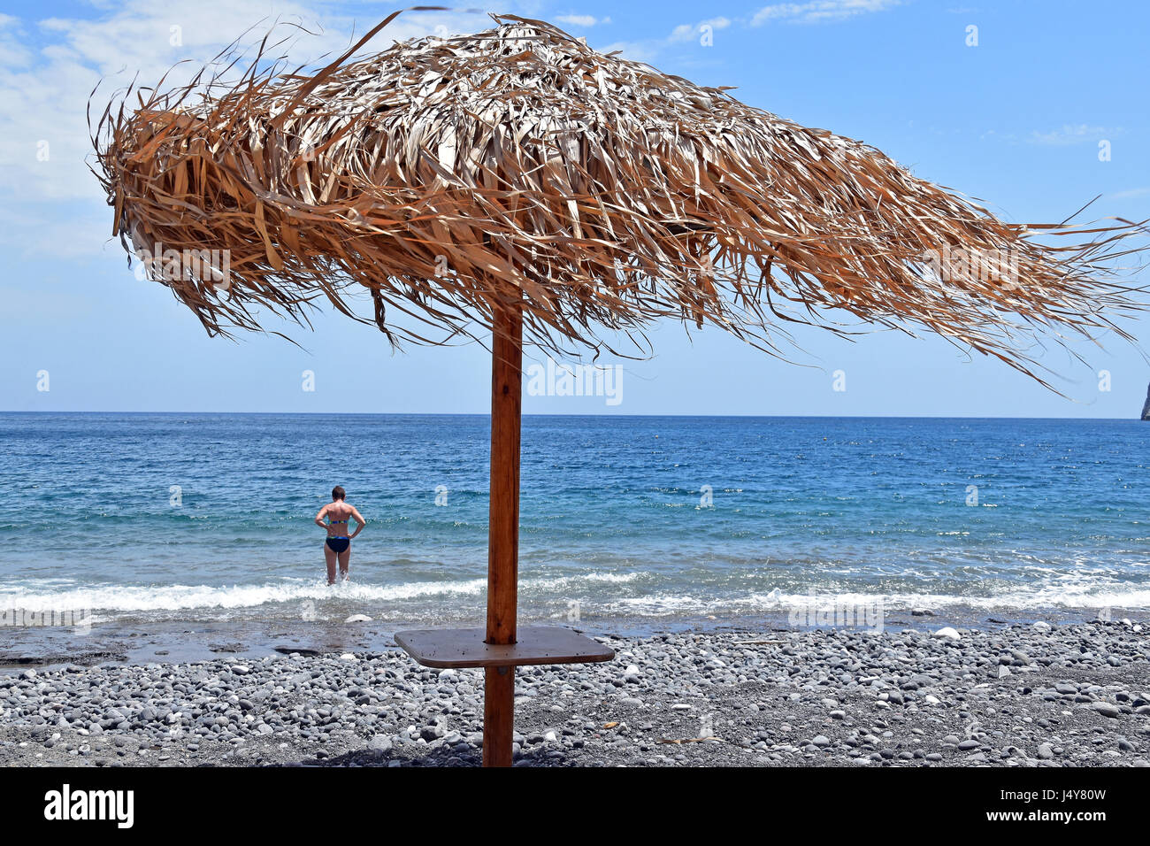Straw parasol blowing in strong winds on Kamari beach, Santorini