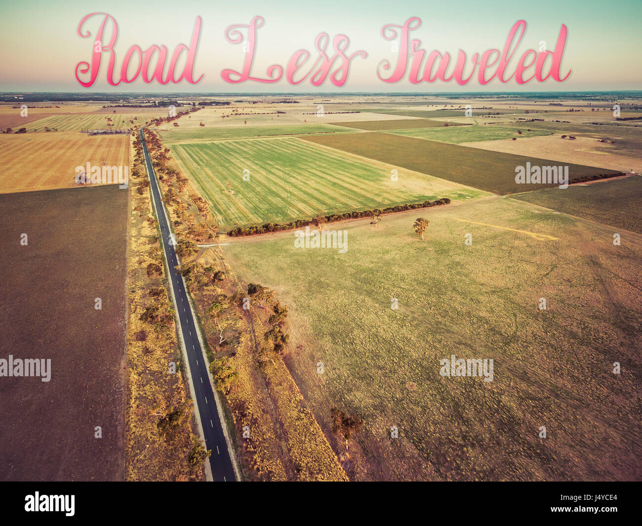 Rural highway passing among agricultural fields into horizon with Road Less Traveled handwritten lettering text Stock Photo