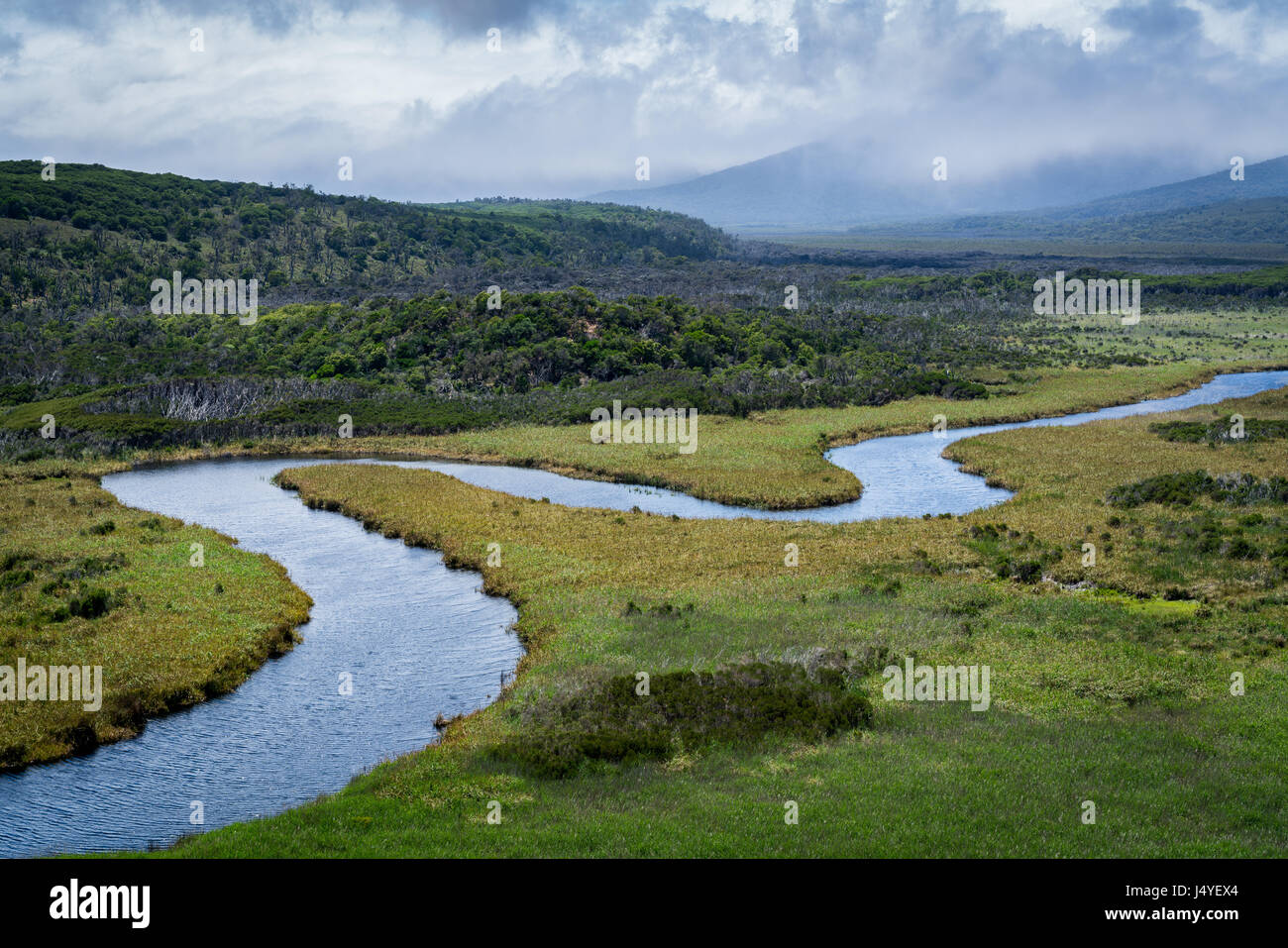 A river serpentines through a plain, with mountains in the background covered by clouds Stock Photo