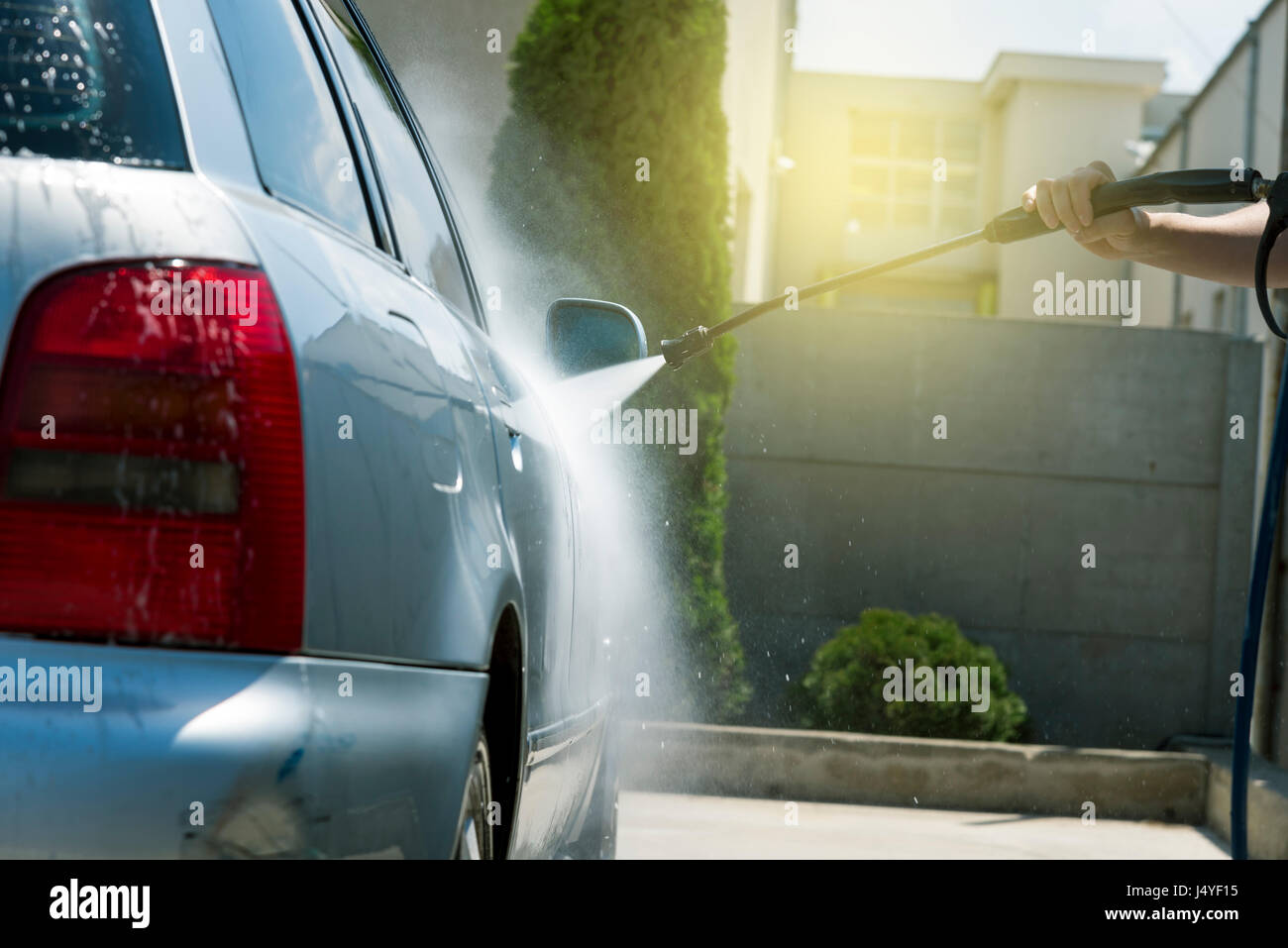Worker in auto service is washing a luxury car by water hoses