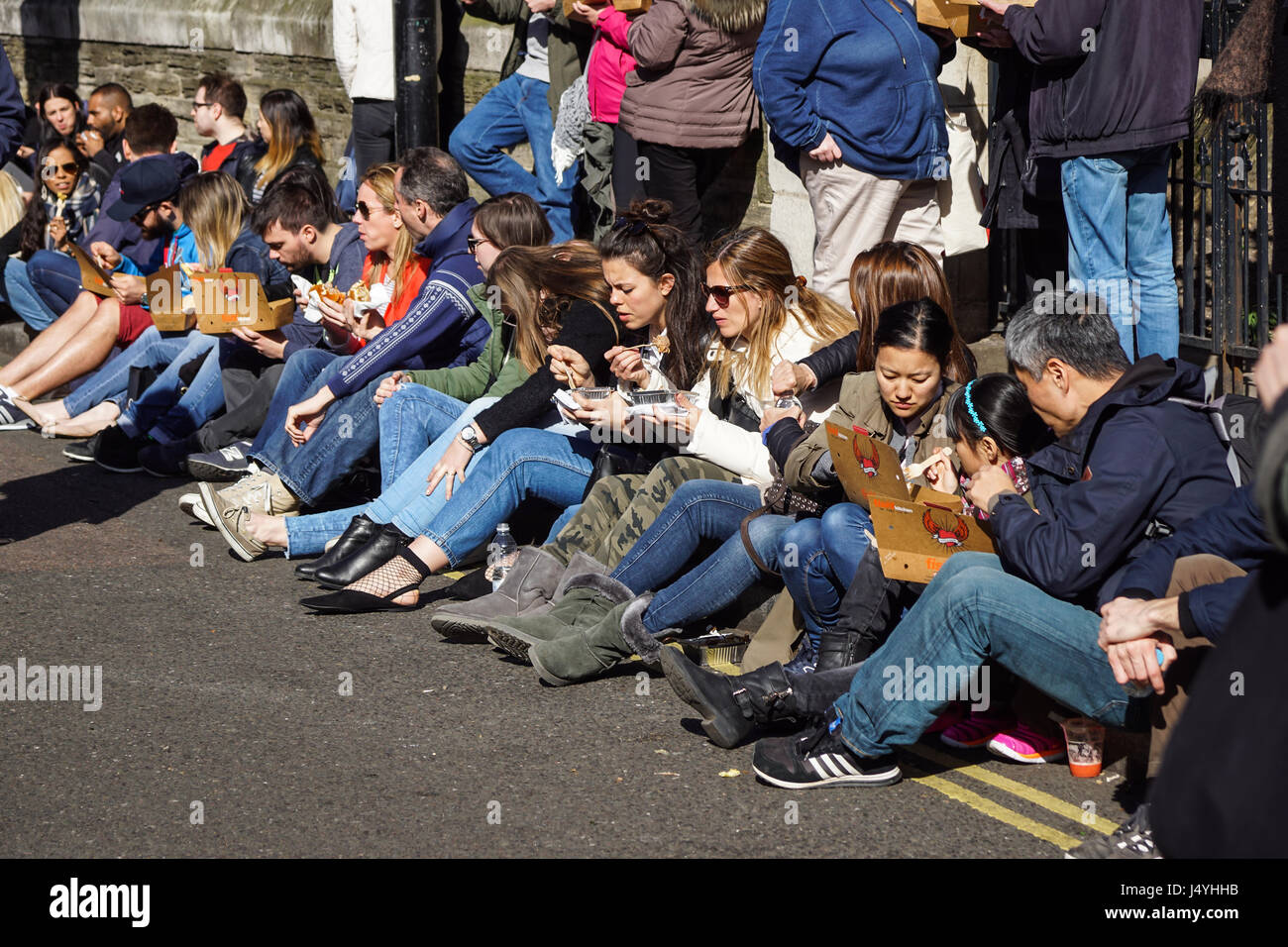 LONDON , APRIL 23 2017: Unidentified A group of people eat a sandwich sitting down the street. During lunch break this is the fastest way to have lunch Stock Photo