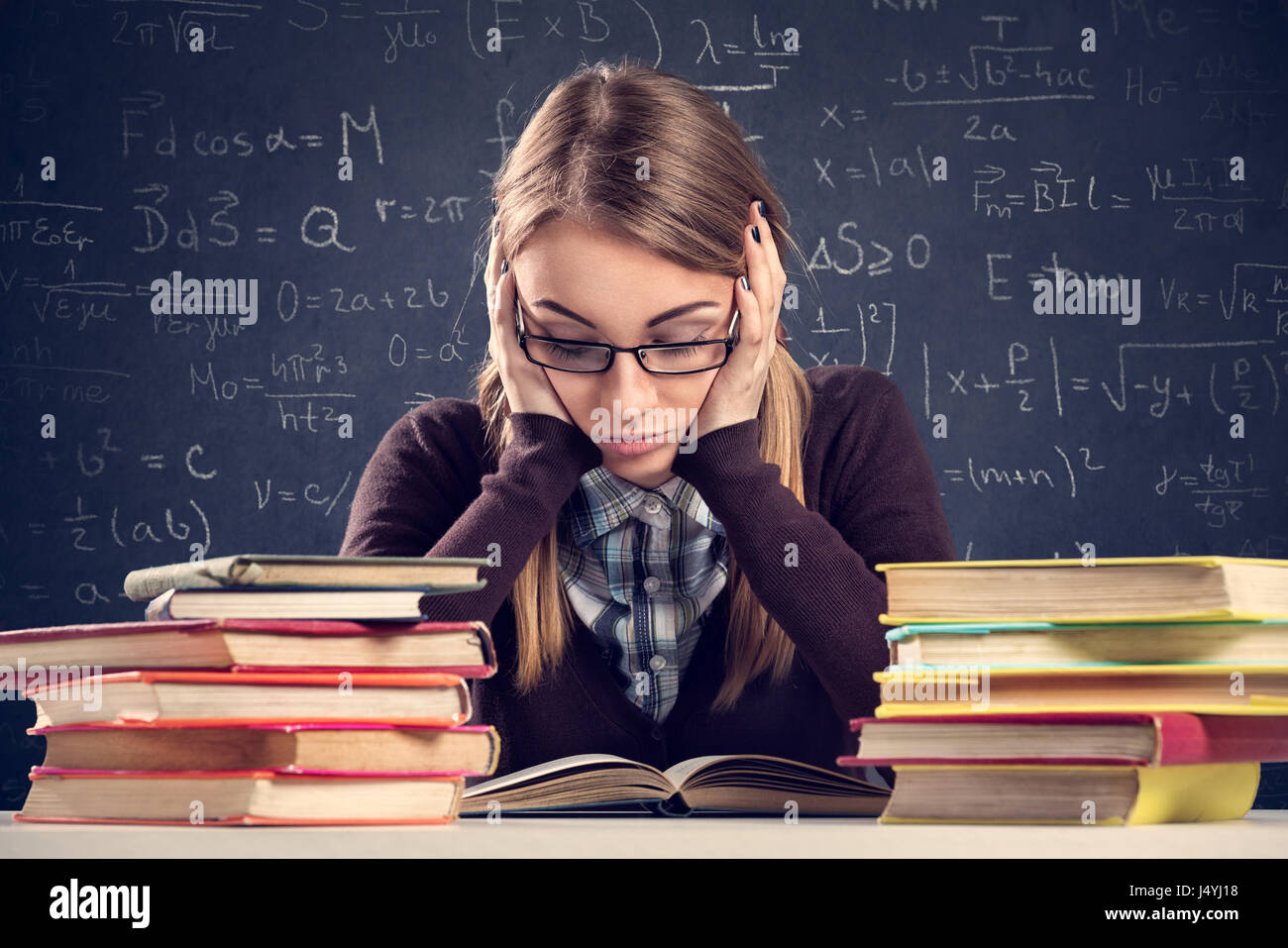 Young student with desperate expression sitting at a desk and looking at her books Stock Photo
