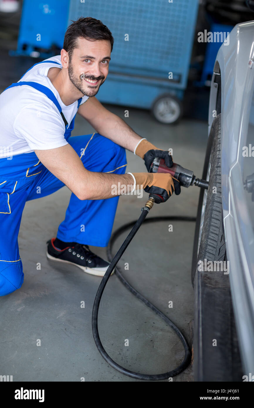 smiling mechanic repairing car wheel in workshop with wrench Stock ...