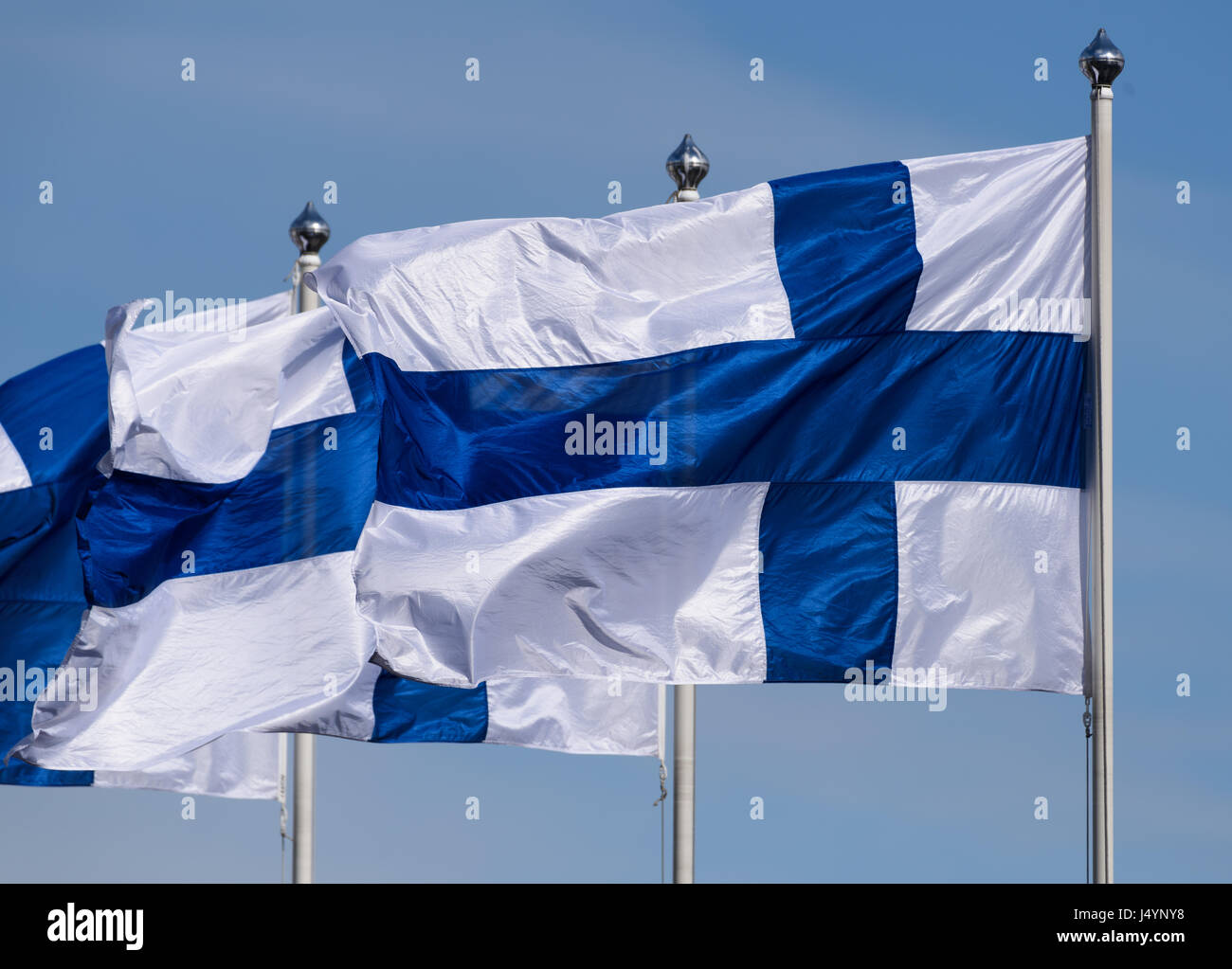 Three Finnish flag flying on sunny spring evening with blue sky in the background Stock Photo