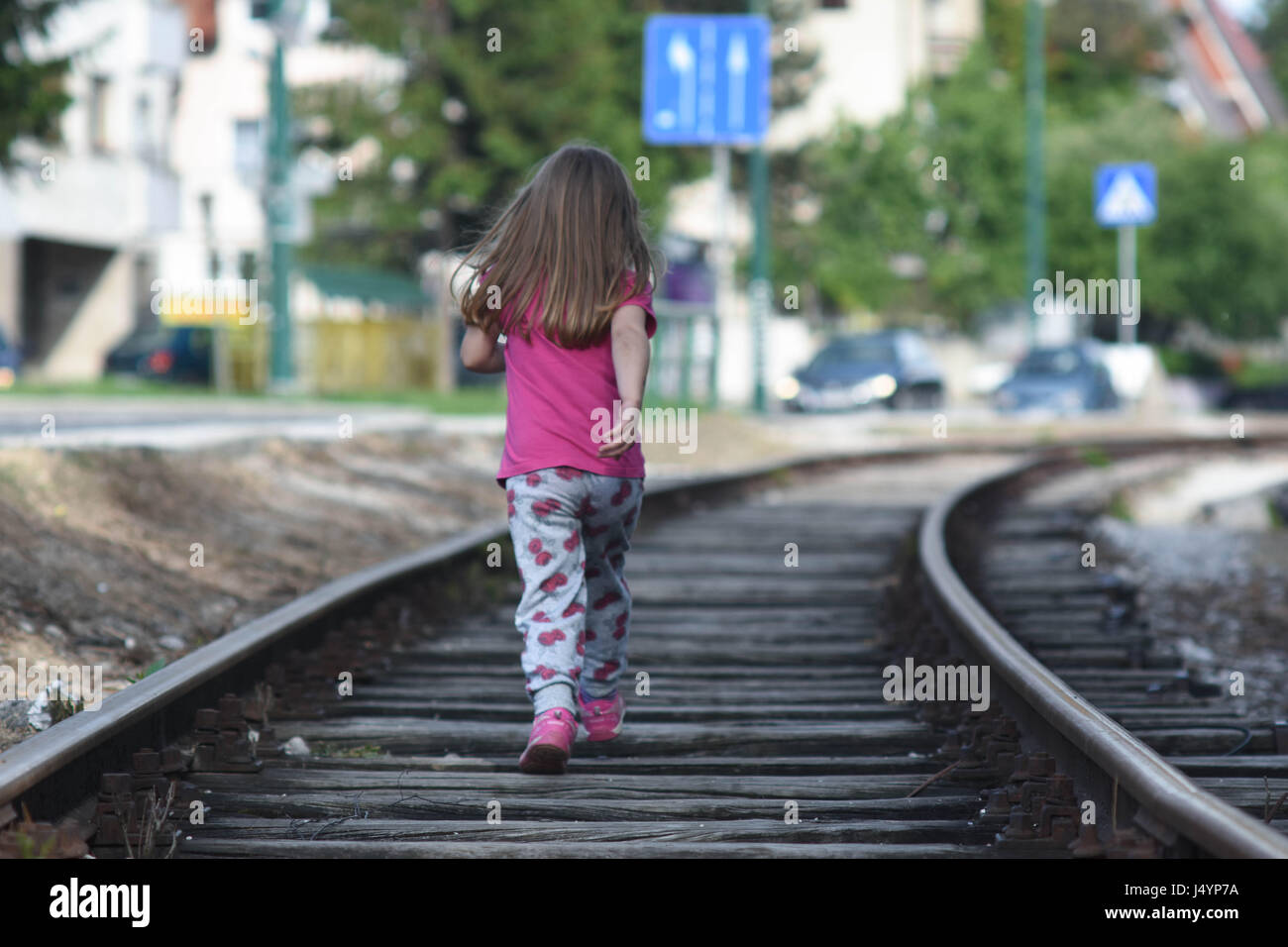 Girl child running on rail road tracks beside street road Stock Photo