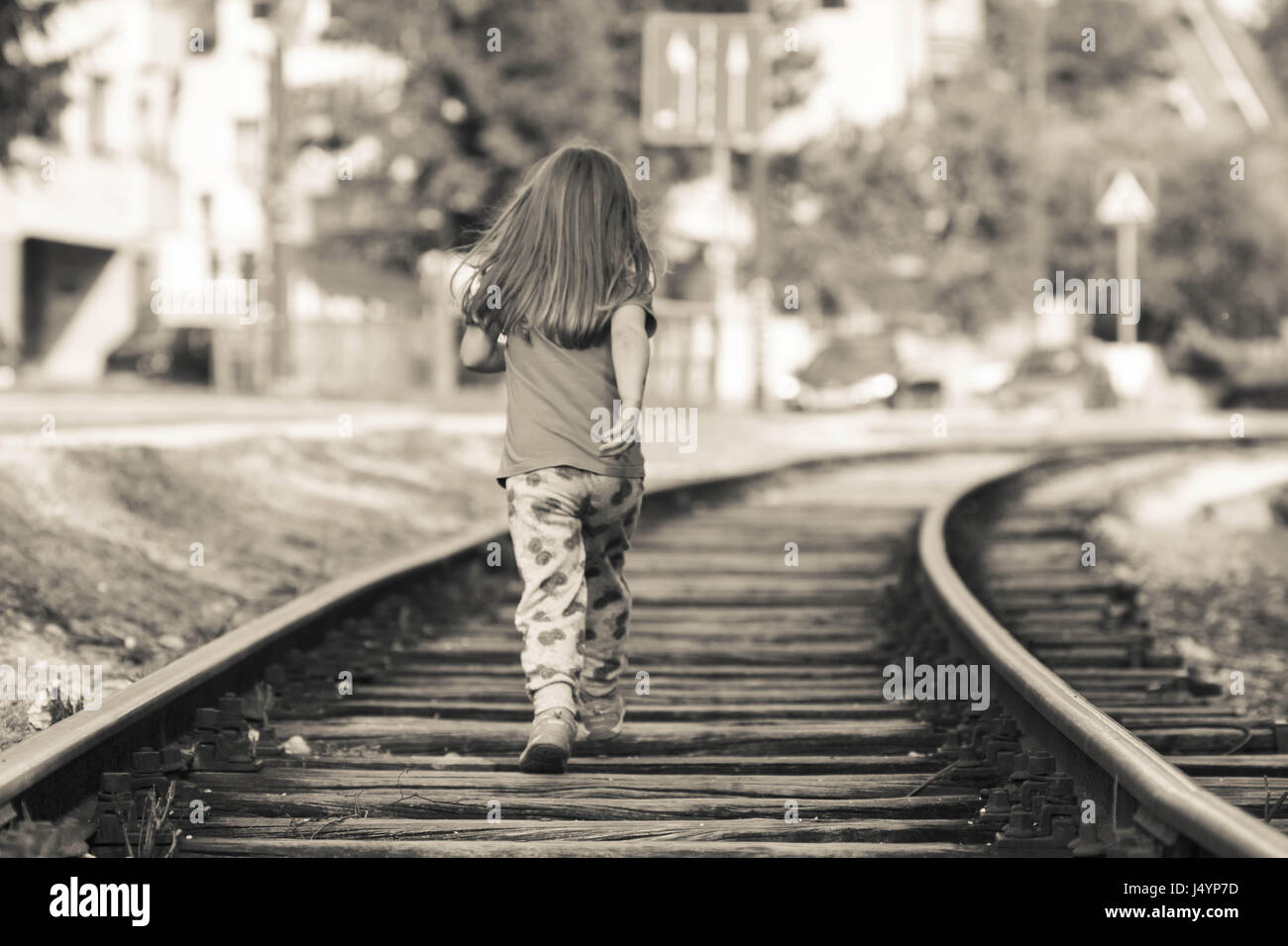 Girl child running on the railroad tracks beside street road Stock Photo