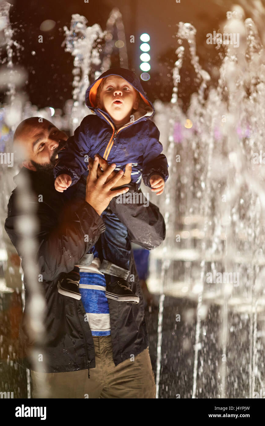Father play with kid in fountain water at night Lima park Stock Photo