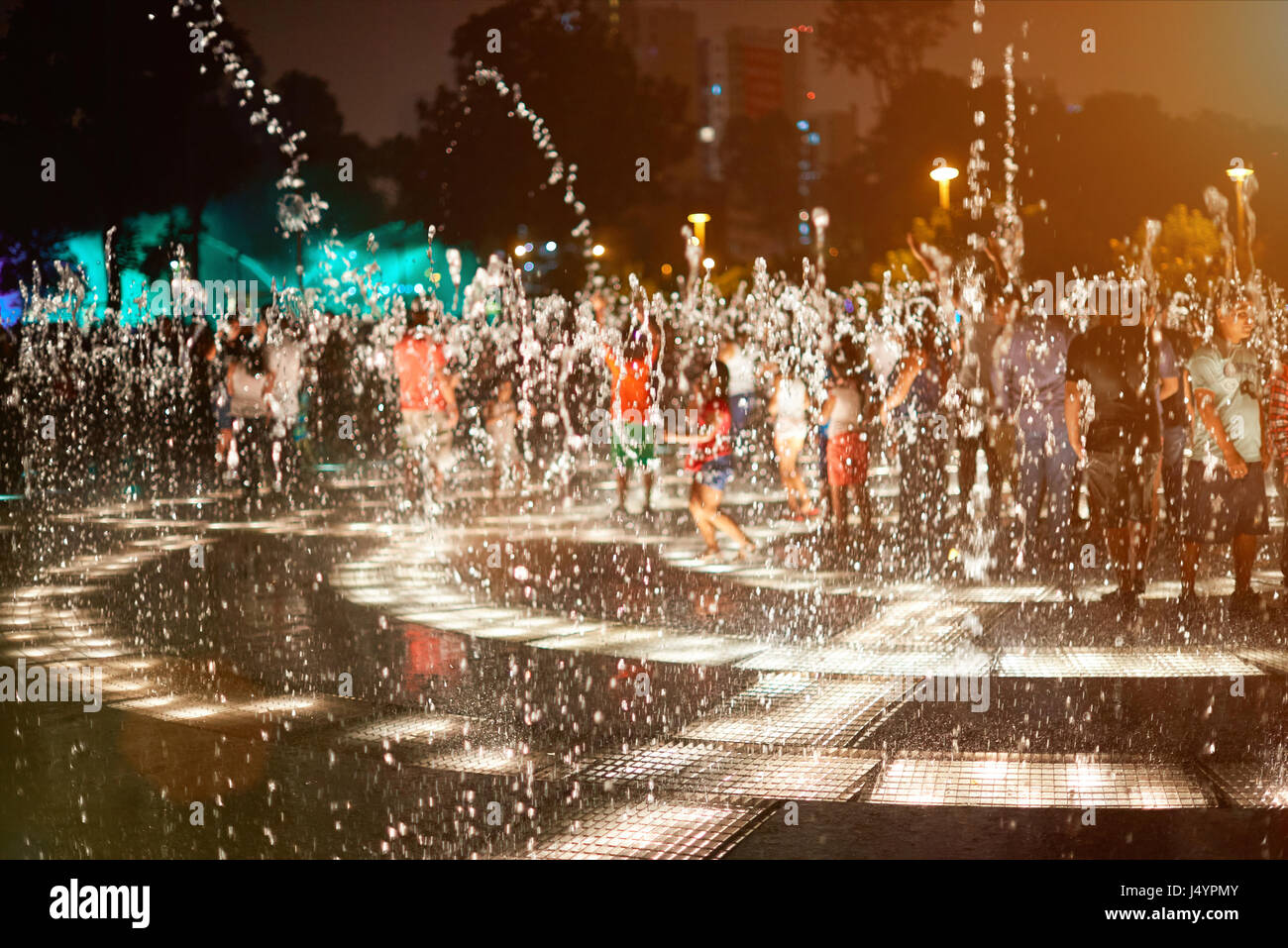 Water fountain splashes at night on blur playing people background Stock Photo