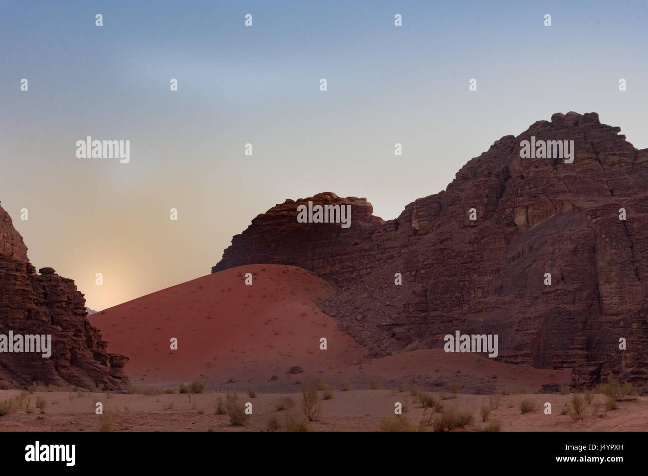 Red sand dune next to rugged rocky mountain in Wadi Rum Desert at sunrise. Stock Photo