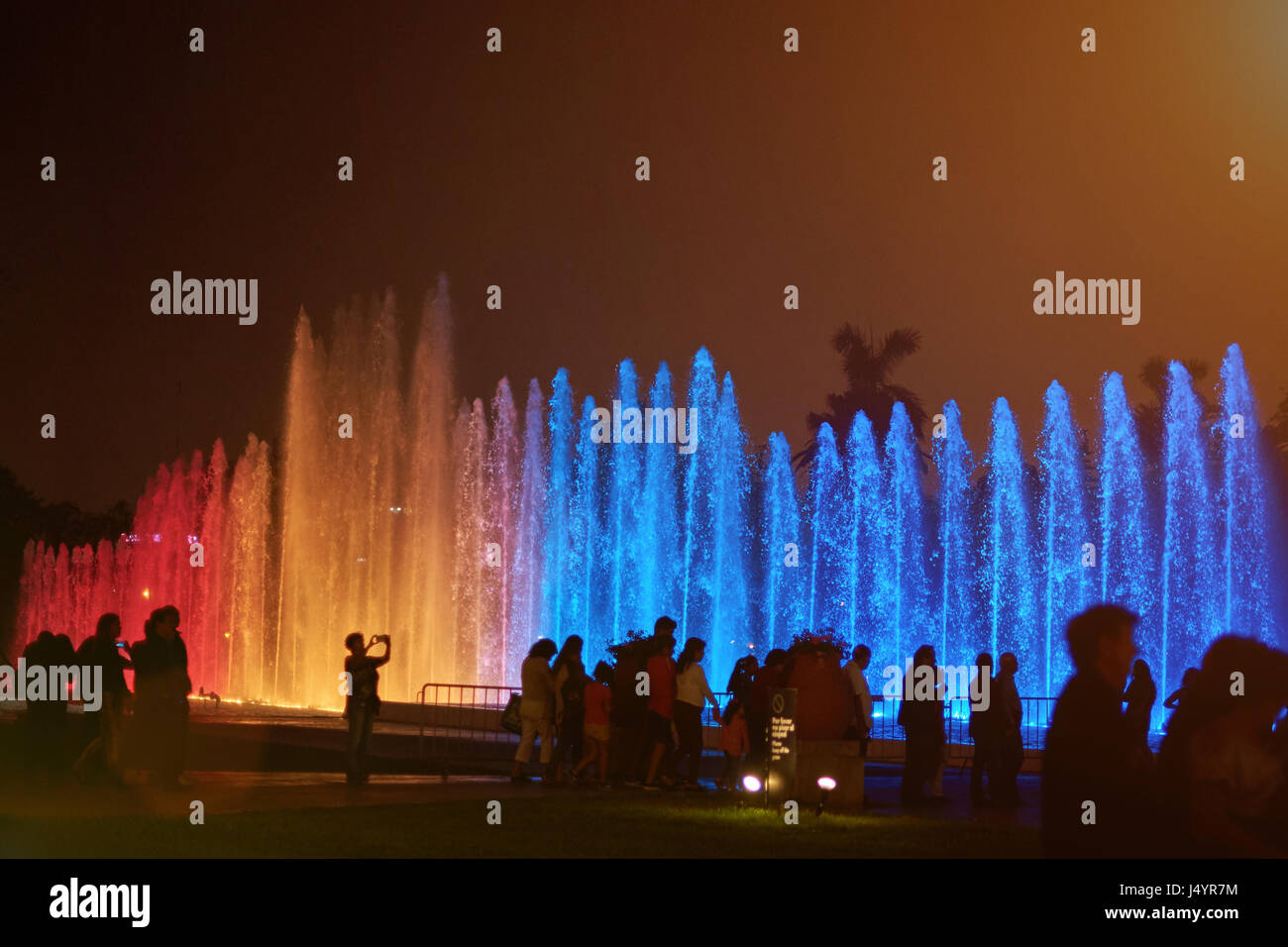 Colorful fountain in Lima park. Silhouette of people walk in park with fountains Stock Photo