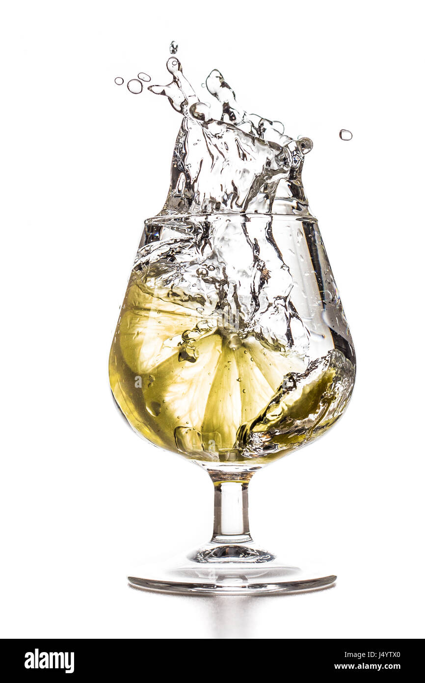 A quarter of lemon is falling into a glass of water with a splash Stock