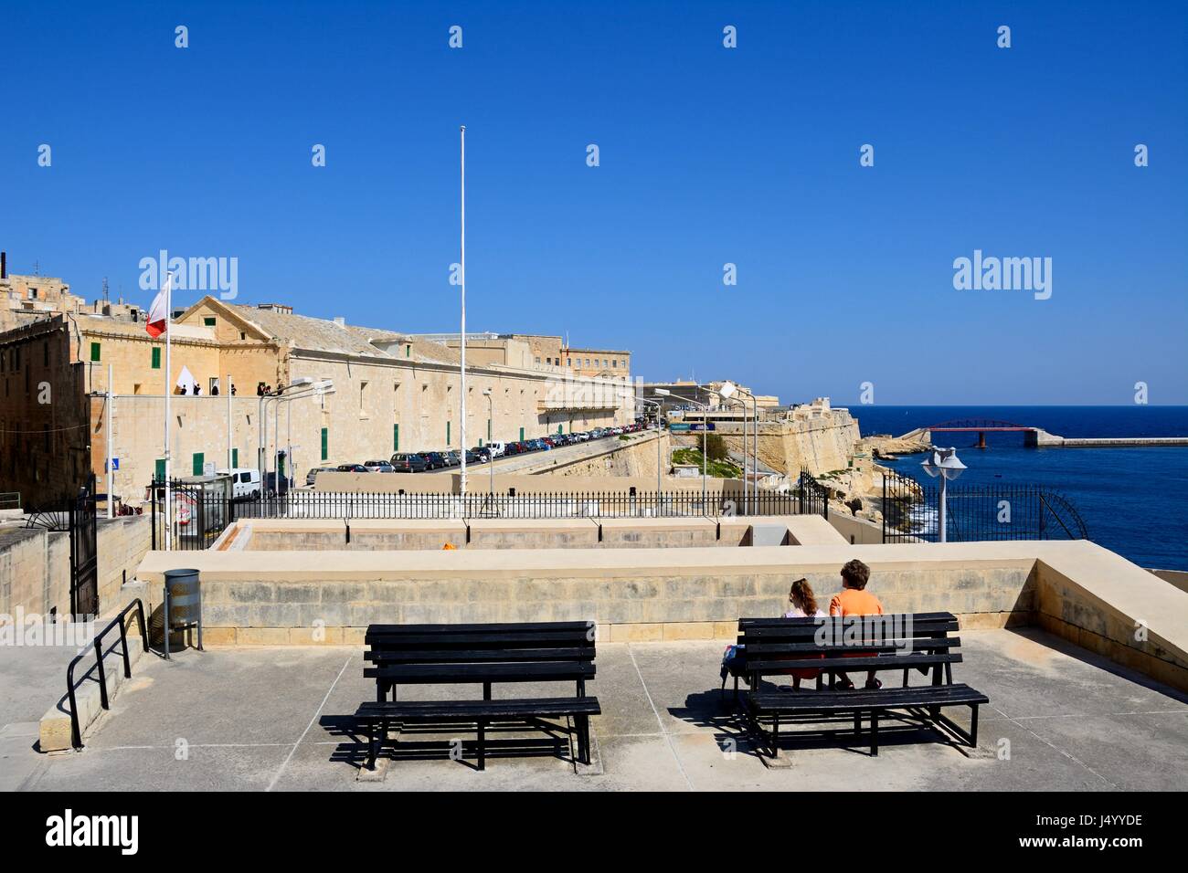View from the Siege Memorial towards north along Triq Il-Mediterran with a couple sitting on a bench looking at the view in the foreground, Valletta,  Stock Photo