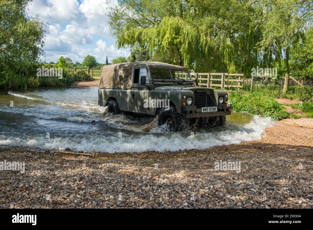 Model released image of a man driving a 1973 ex army Land Rover Series 3 Long Wheel Base into the river VER which forms a ford at Redbournbury, Herts. Stock Photo