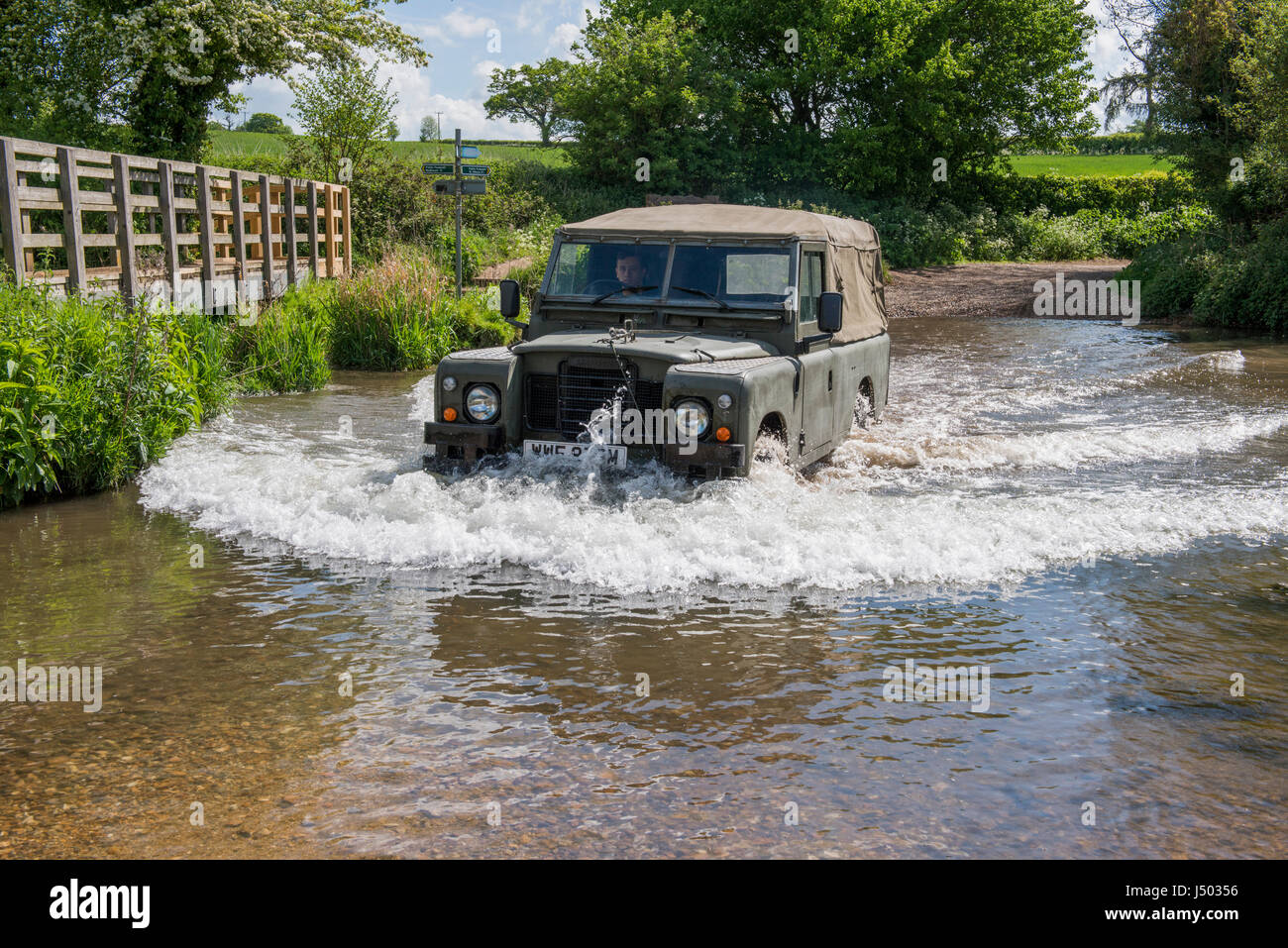 Model released image of a man driving a 1973 ex army Land Rover Series 3 Long Wheel Base into the river VER which forms a ford at Redbournbury, Herts. Stock Photo