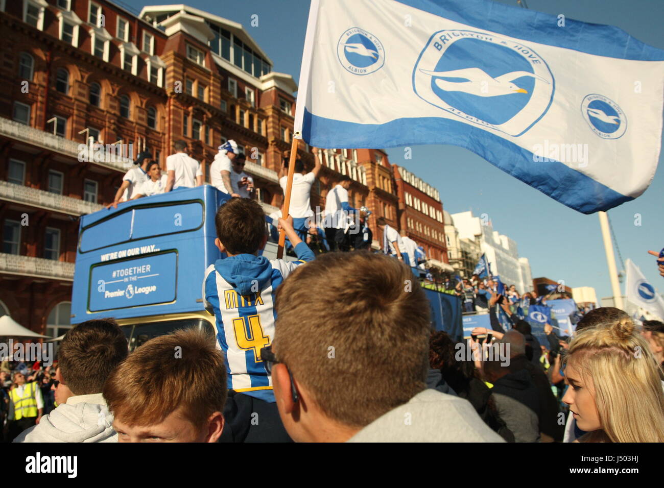 Brighton, UK. 14th May 2017.  A young boy flies a flag with Brighton and Hove Albion colours on it, while sitting on his father's shoulders. Fans of Brighton and Hove Albion Football Club Came out in their thousands to watch the team's bus-top parade along the city's coast road. Team and fans were celebrating promotion to the Premiership. Roland Ravenhill/ Alamy Live News Stock Photo