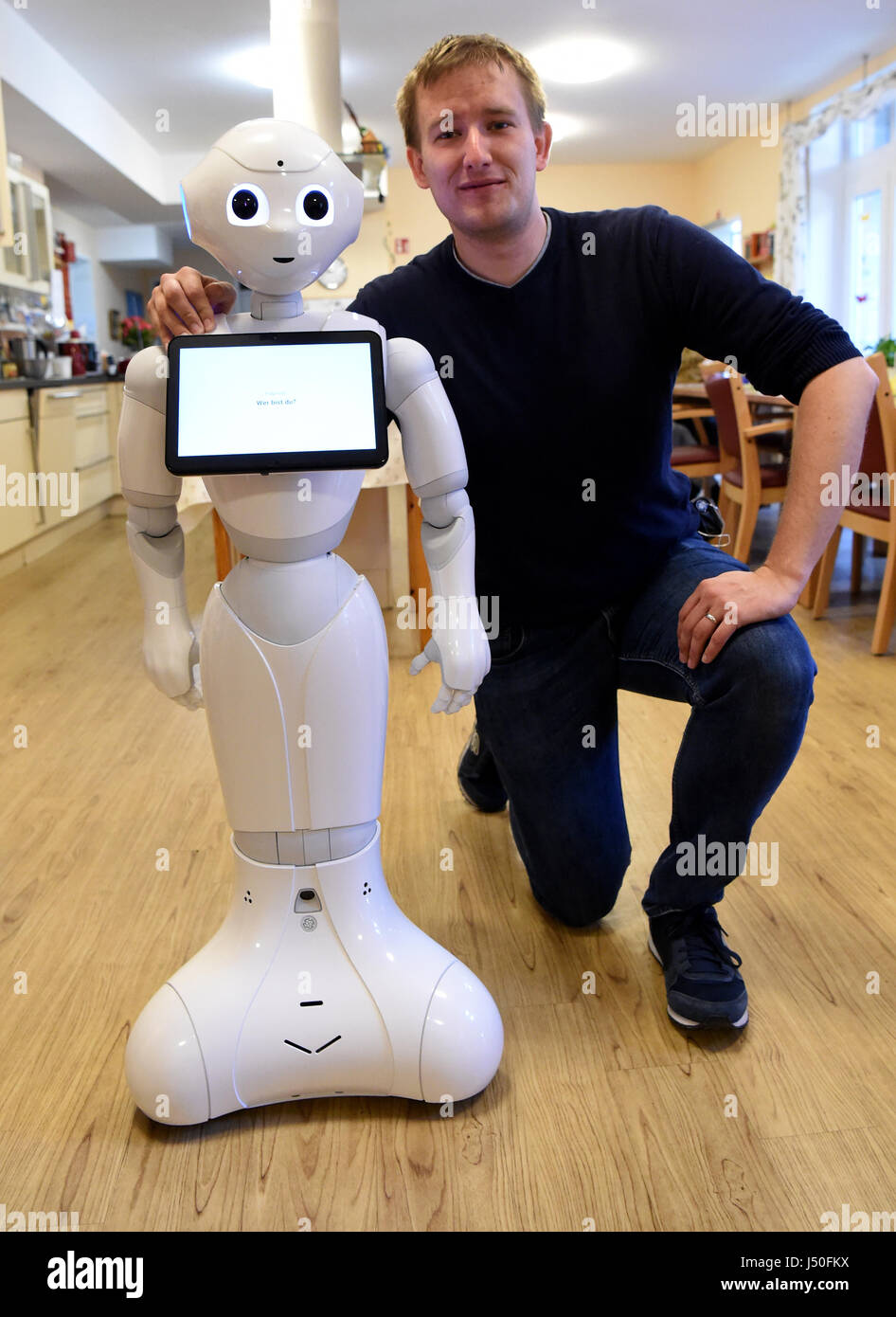 Kiel, Germany. 11th May, 2017. Robotics engineer Hannes Eilers from Kiel University of Applied Sciences kneeling beside 'Emma' the robot, which he programmed, in Kiel, Germany, 11 May 2017. The robot can speak, play music and take photographs of residents on demand. Photo: Carsten Rehder/dpa/Alamy Live News Stock Photo