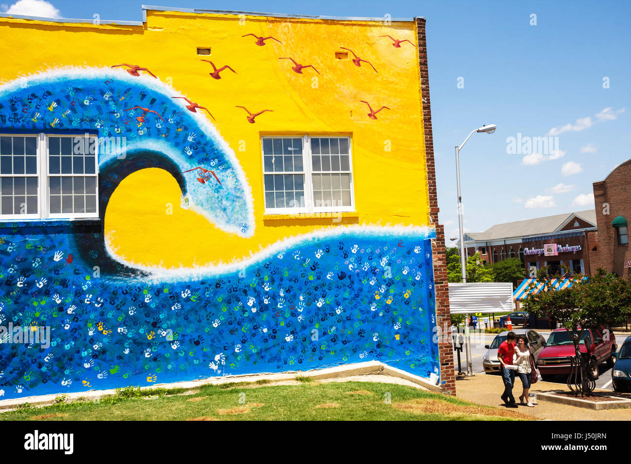Auburn Alabama,North College Street,male,female,student students couple,college town,building mural,yellow,blue,waves,water,seagulls,handprints,public Stock Photo