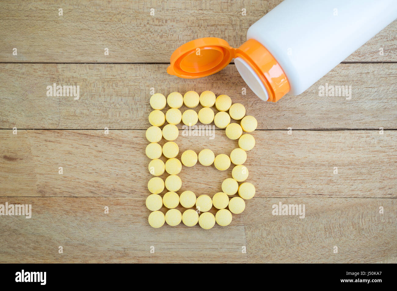 Yellow pills forming shape to B alphabet on wood background Stock Photo